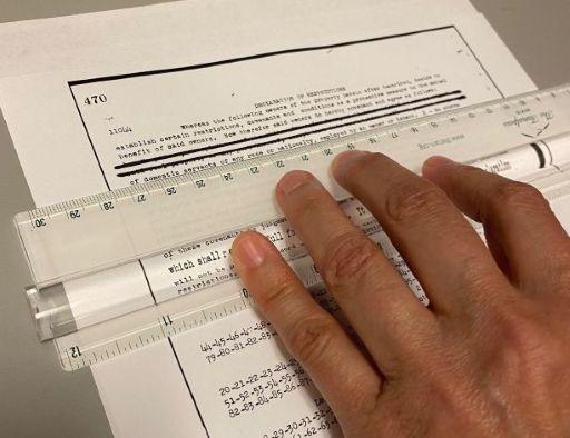 Person's hand on a ruler over a piece of paper with some of the text stricken through with black ink.