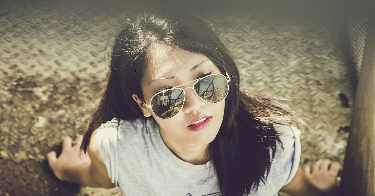 A young woman wearing sunglasses sits in the sun on what appears to be a hot day.