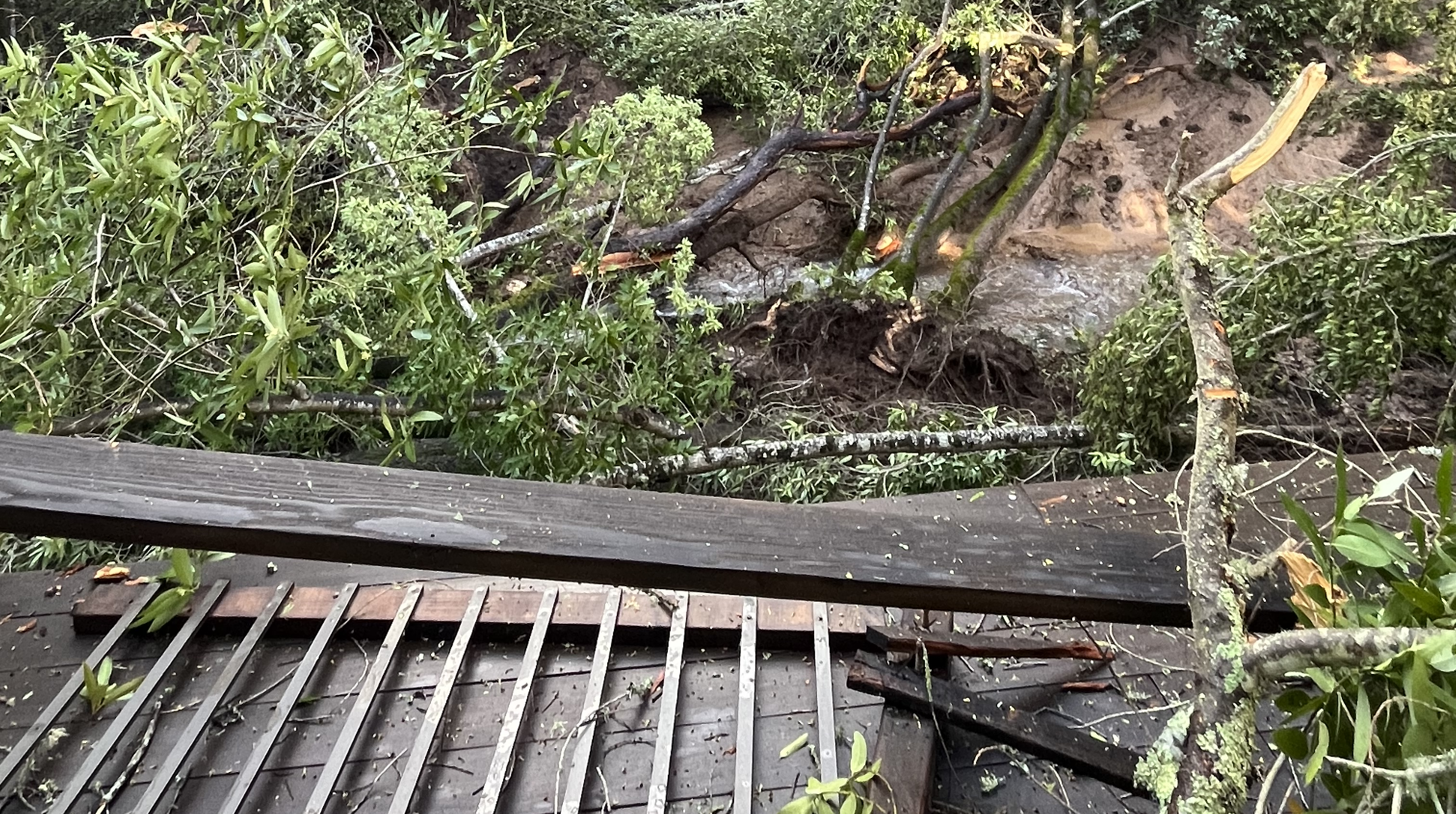 A closeup view of a backyard deck destroyed by a mudslide, with debris in the background.