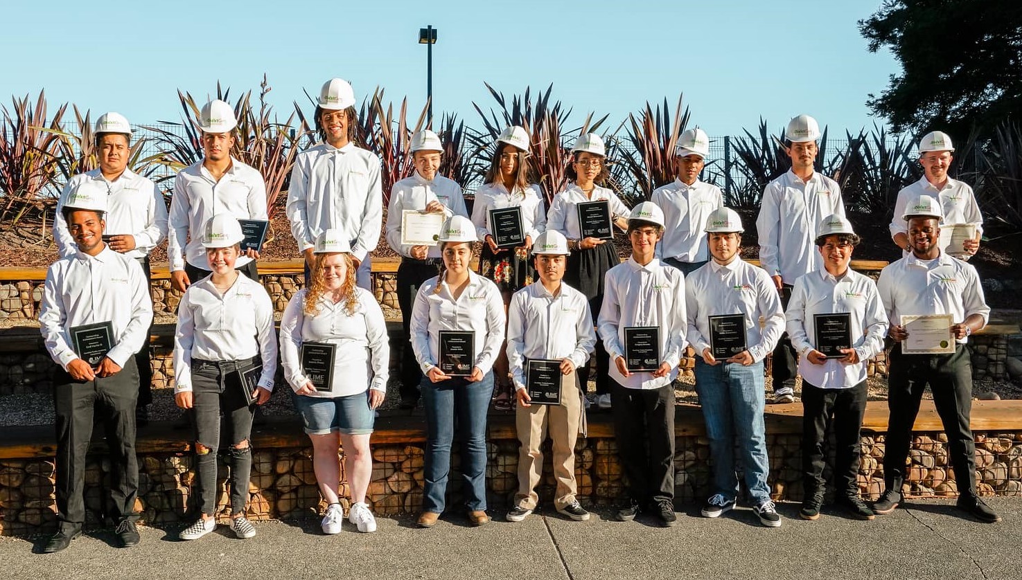 About 20 young people wearing hardhats pose with their certificates after construction training.