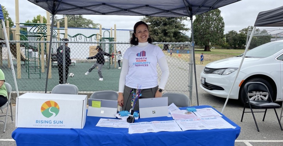 A smiling woman stands under a tent and behind a table with information about energy saving efforts at home.