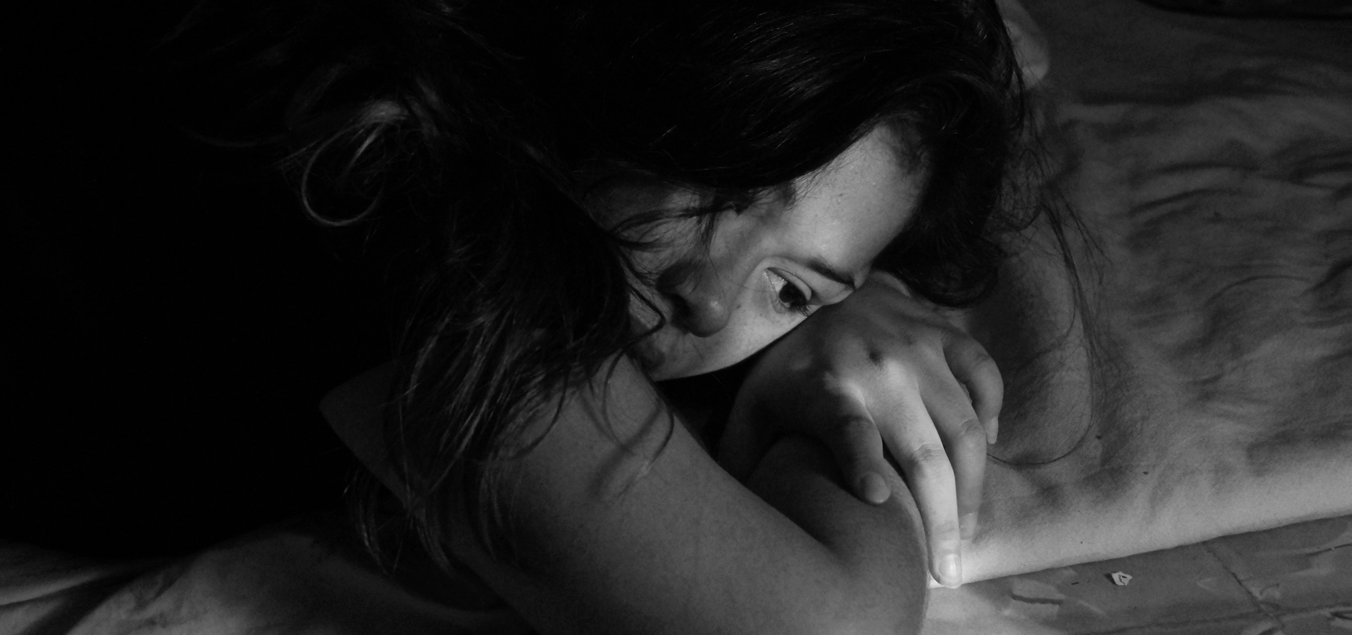 A young woman appears sad as she lays on a bed.