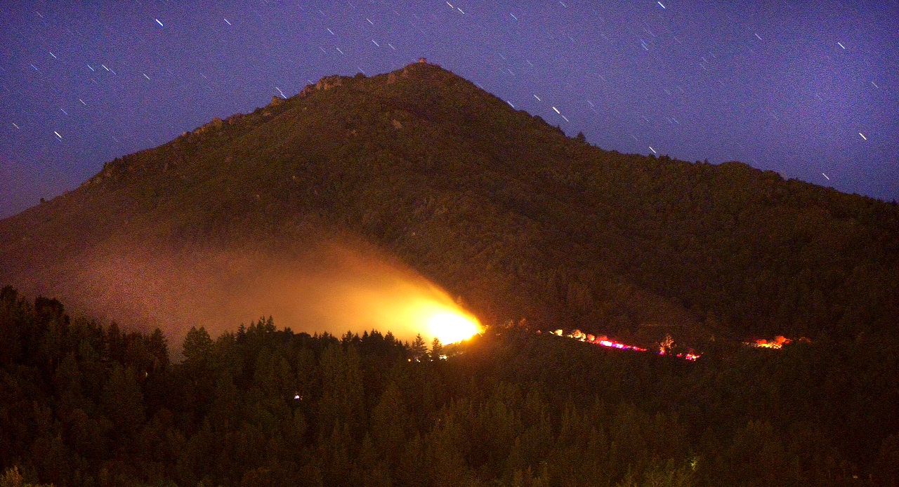 A wildfire burns at night with a mountain in the background.