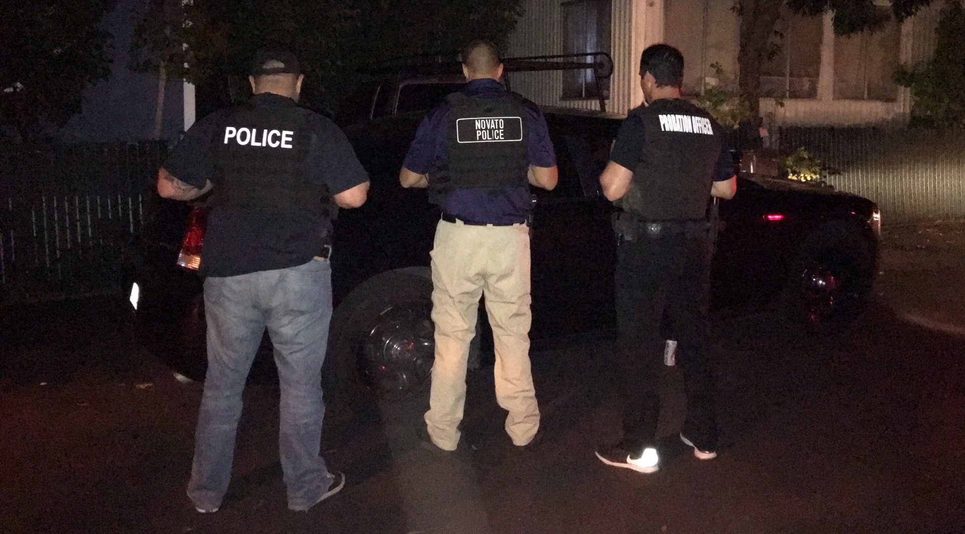 Three law enforcement officers stand in the dark during a compliance check.