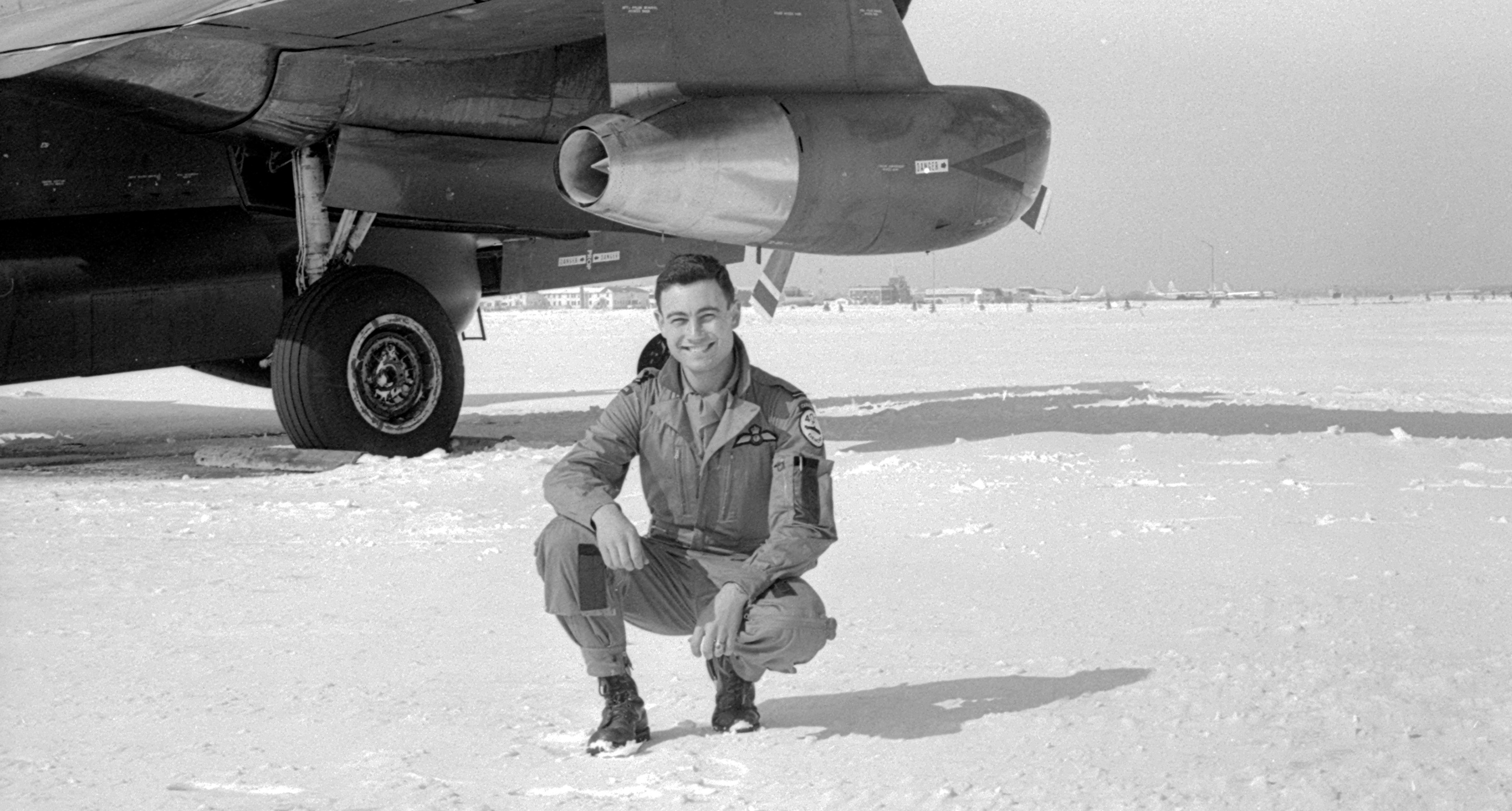 A photo of Rick Saber from the 1960s, kneeling down on snow next to an airplane.