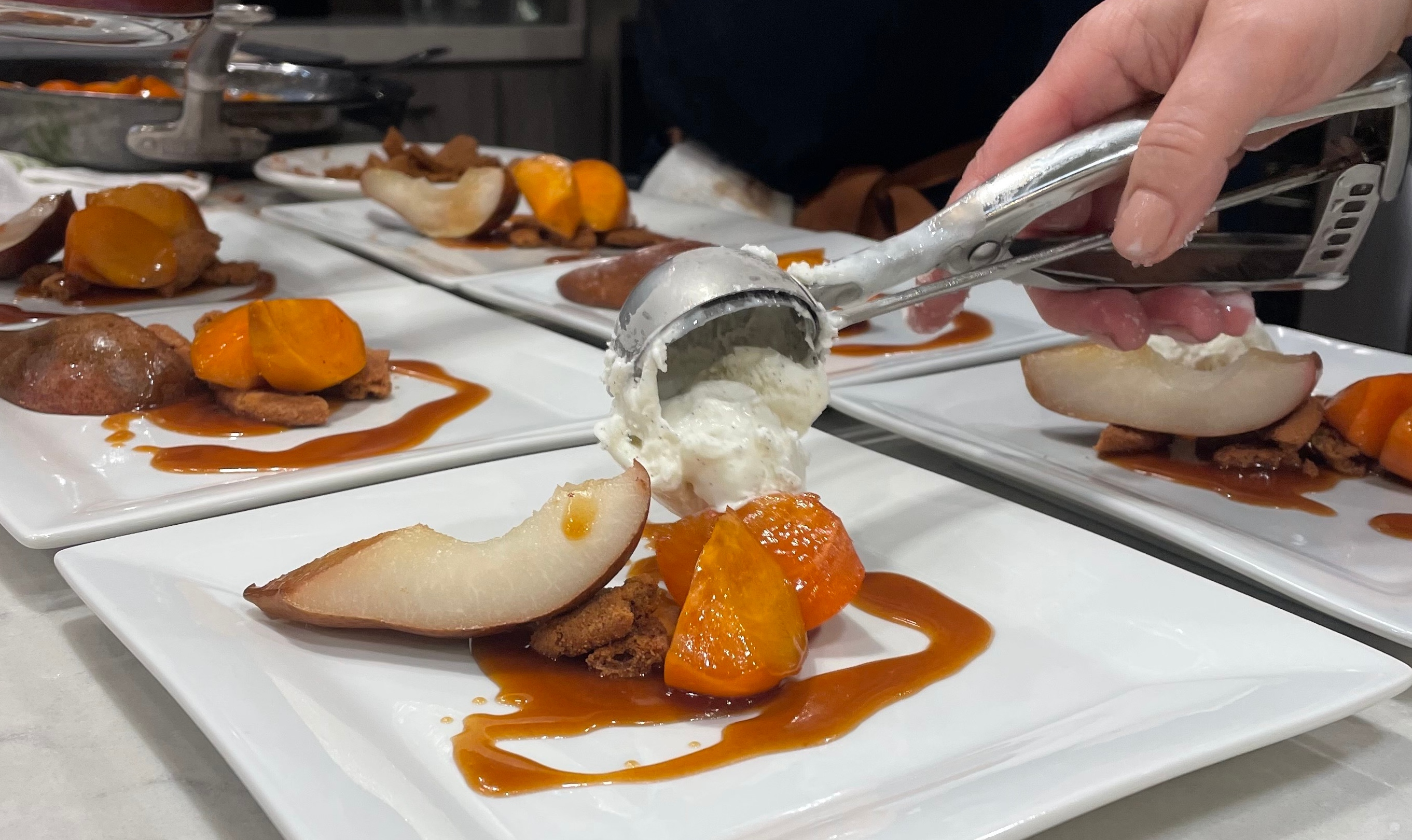 A closeup view of a chef's hand scooping dessert onto a plate.