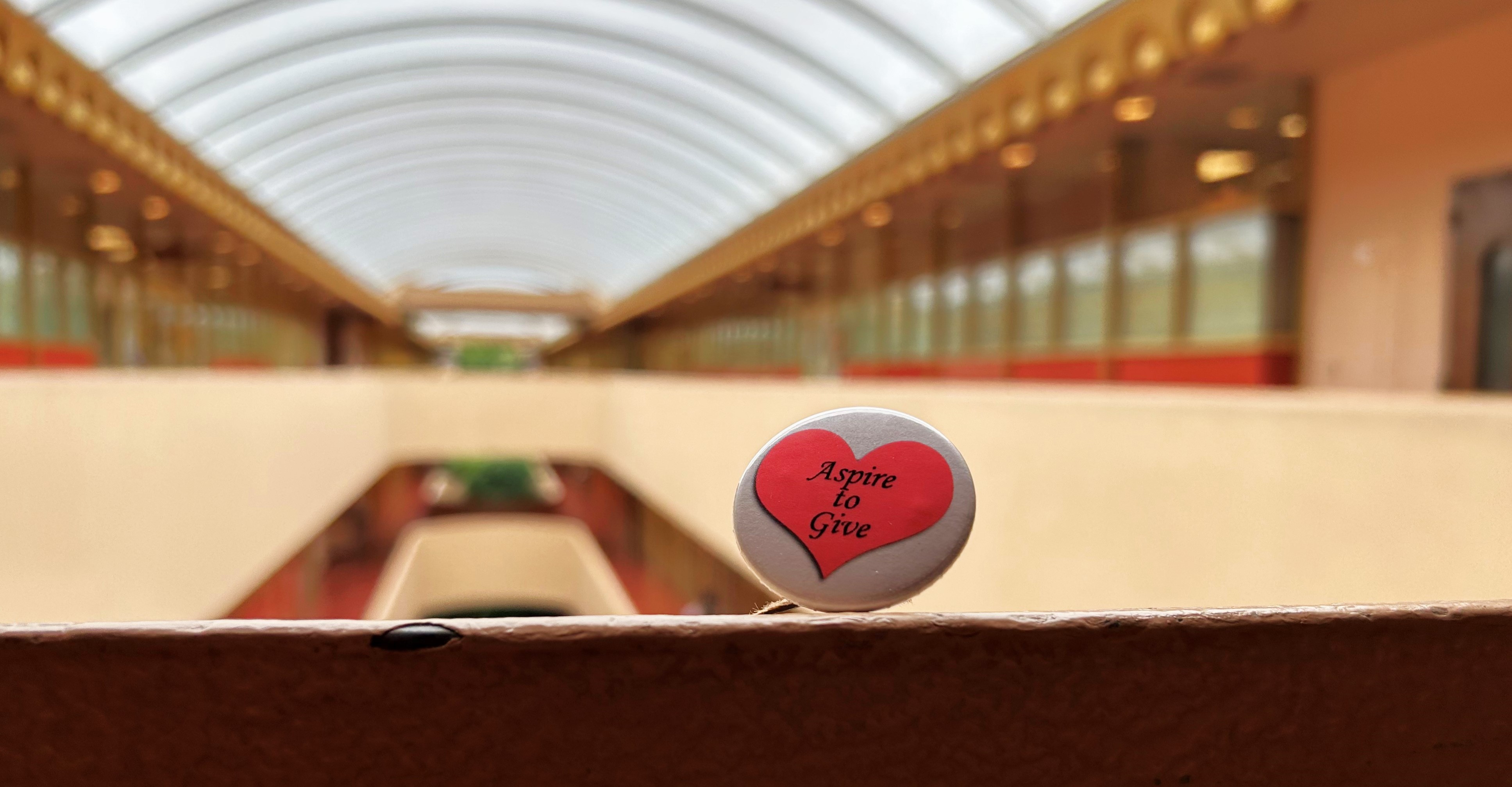 A closeup view of a button that says Aspire to Give sitting on a ledge in the Civic Center hallway.