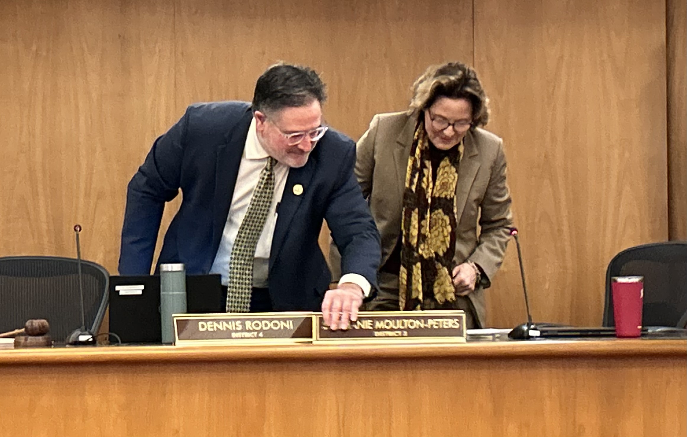 Dennis Rodoni exchanges name plaques with Stephanie Moulton-Peters, signifying the change in position. 
