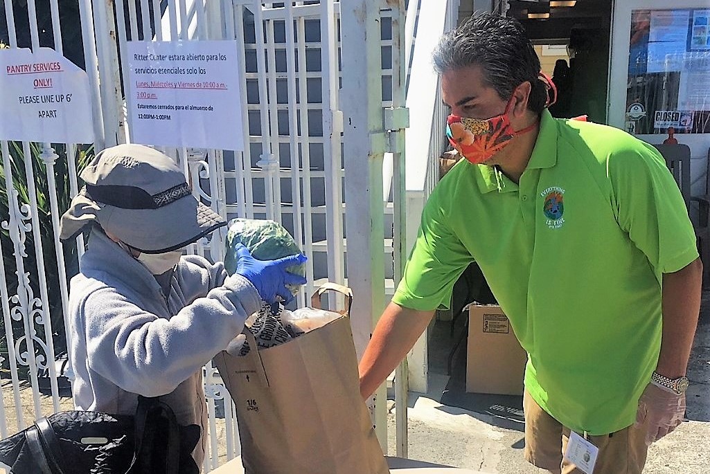 A woman picks up a bag of goods as a volunteer worker assists.
