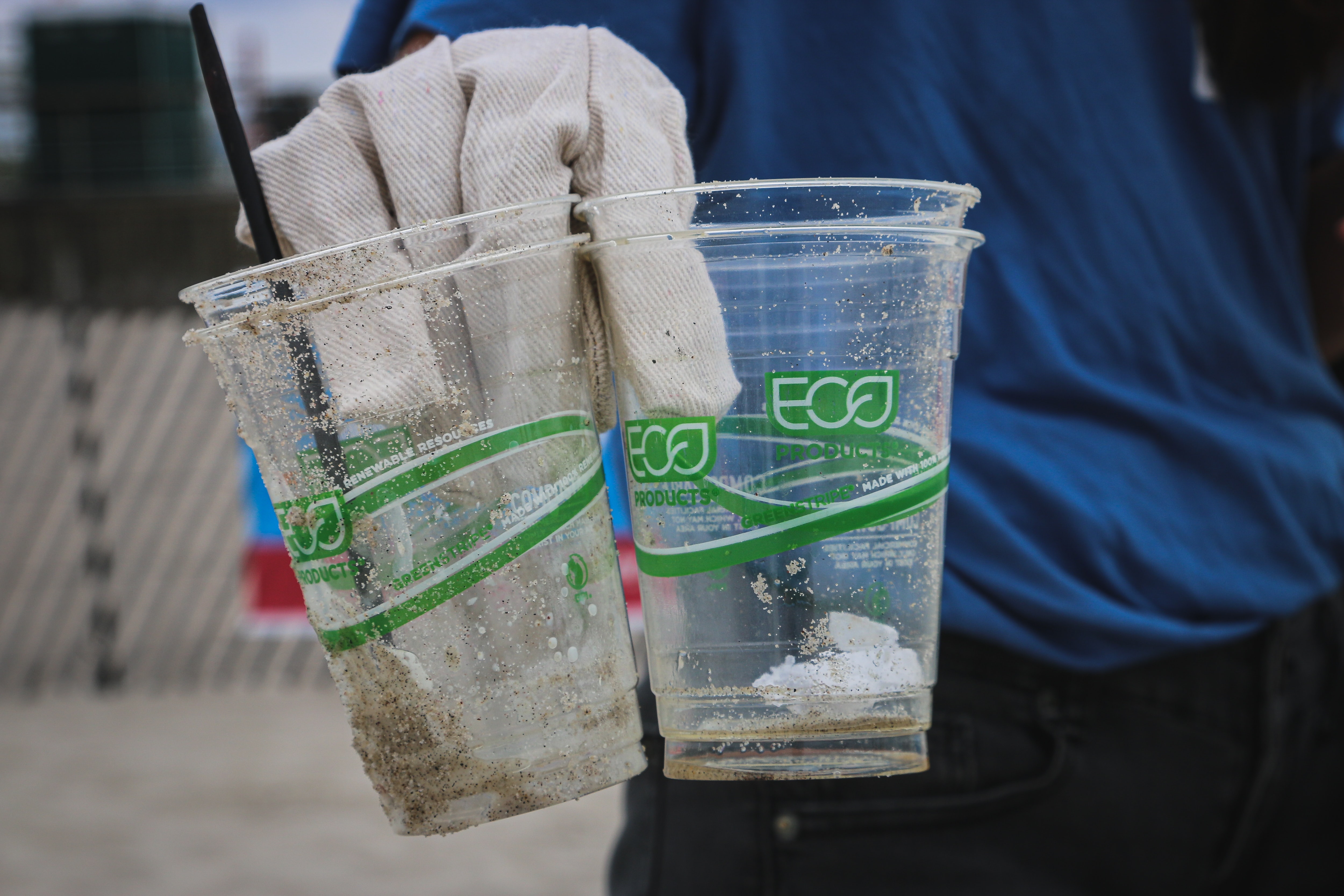 A closeup of someone's gloved hands holding plastic cups picked up as trash.