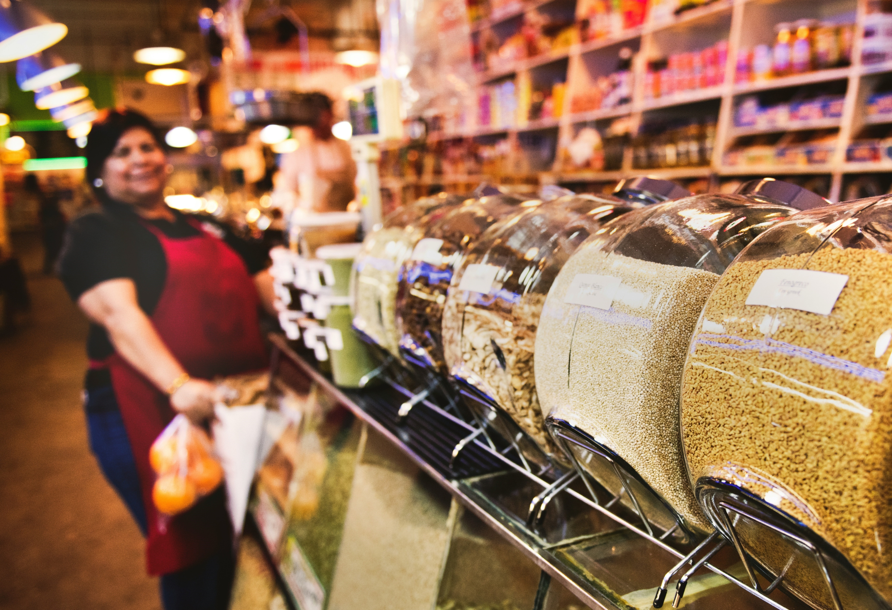 A female store clerk stands in front of small glass bins of foods.