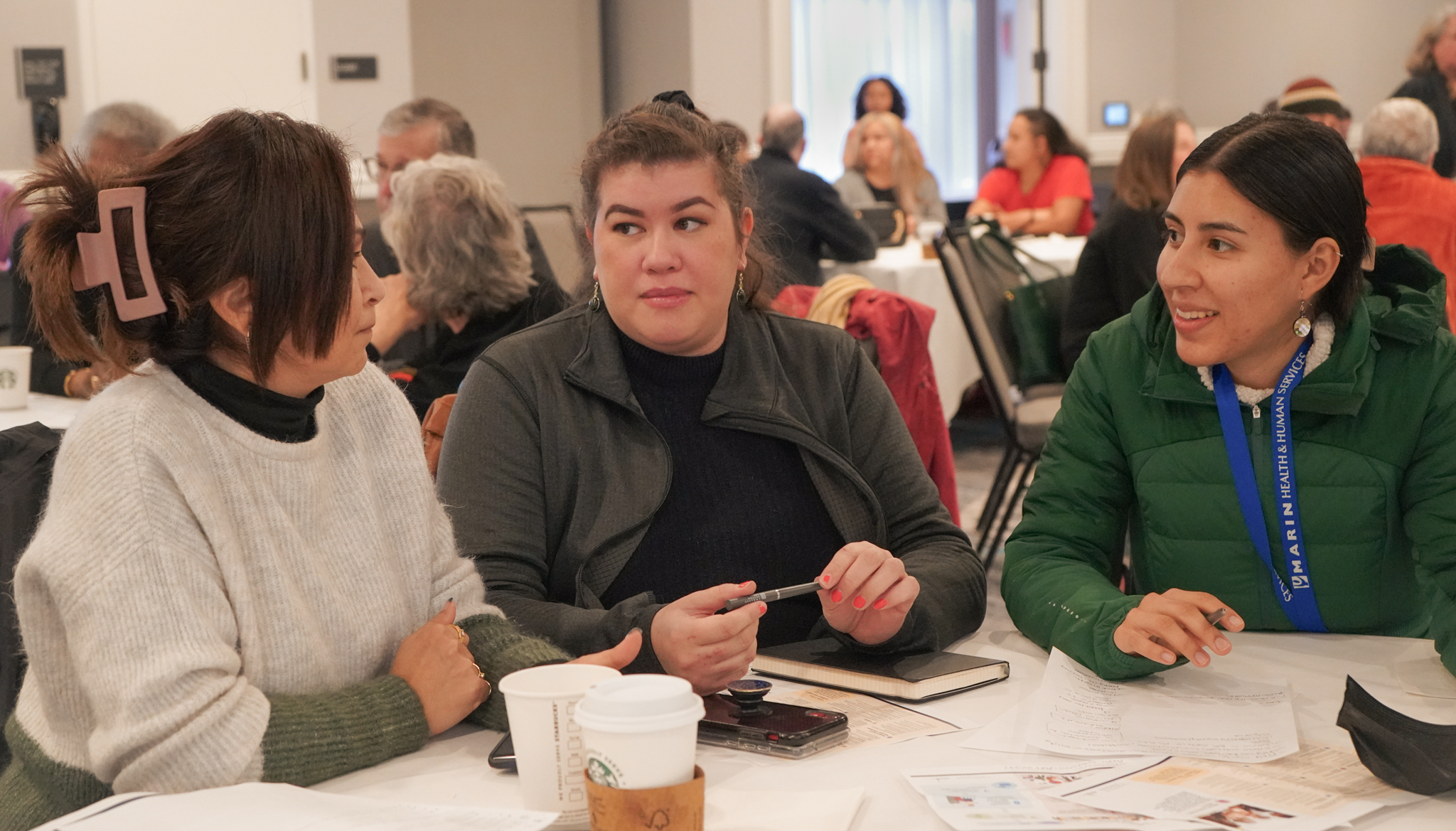 Three people sit at a table during a Participatory Budgeting discussion.