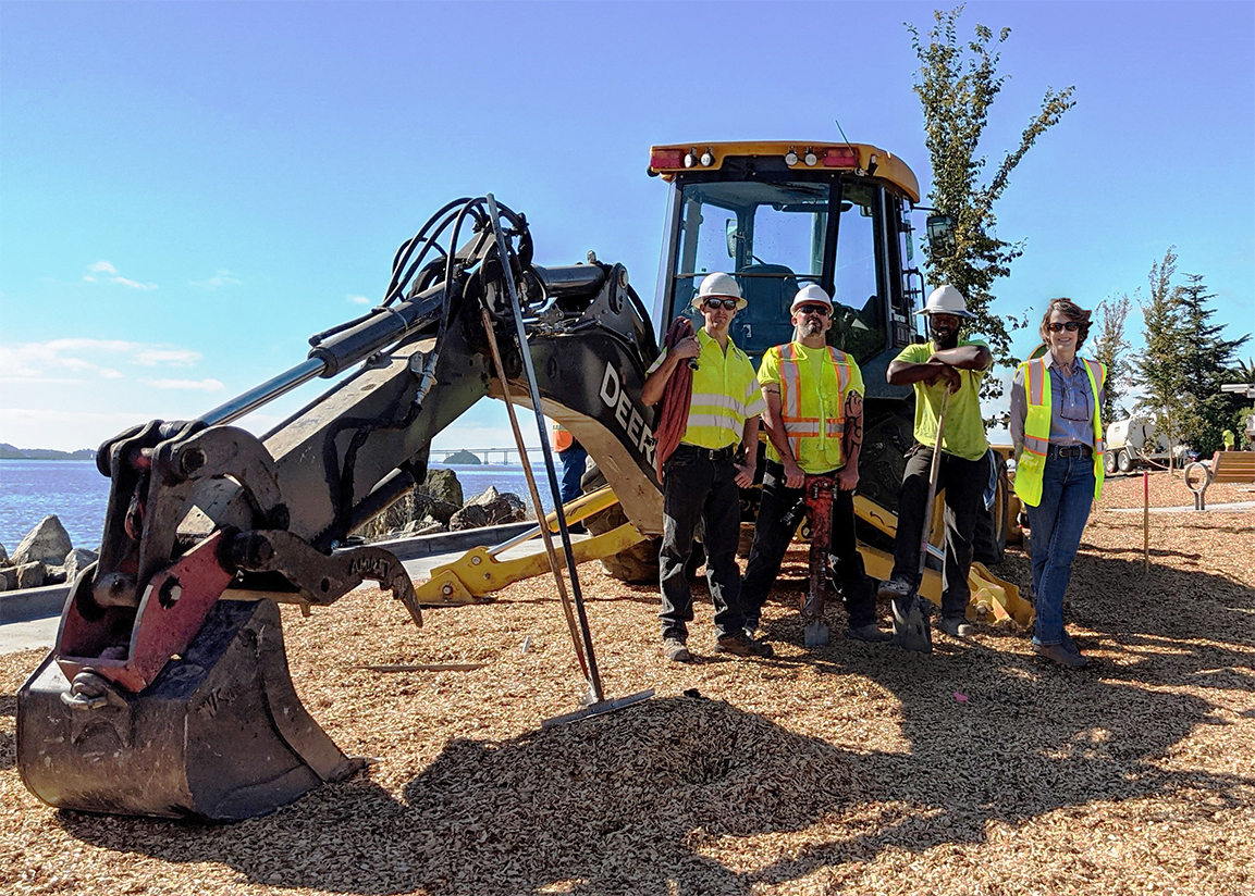 Four construction workers stand net to a piece of heavy equipement.