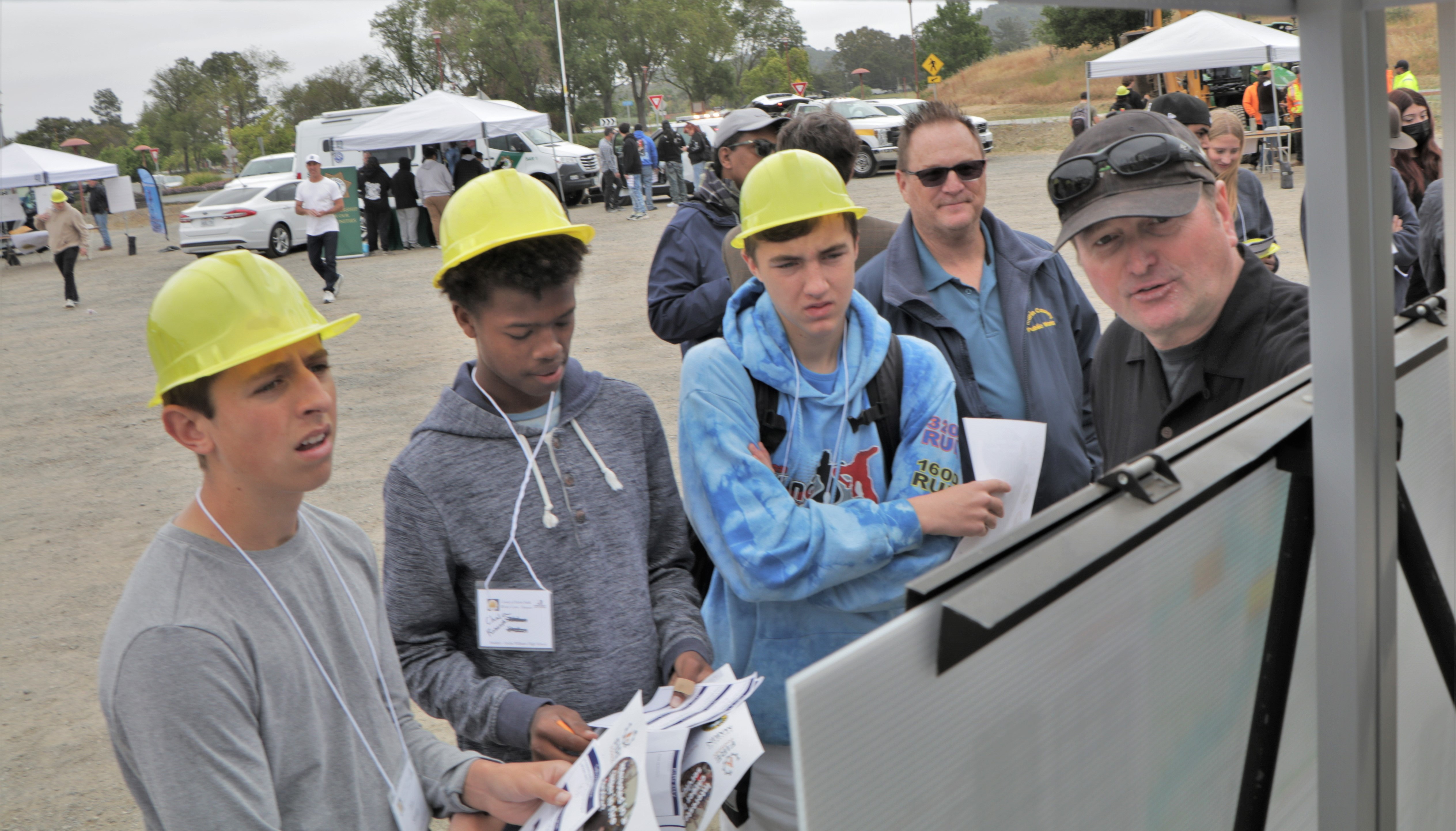 A male Public Works engineer, right, speaks with three teenage boys at a career fair. 