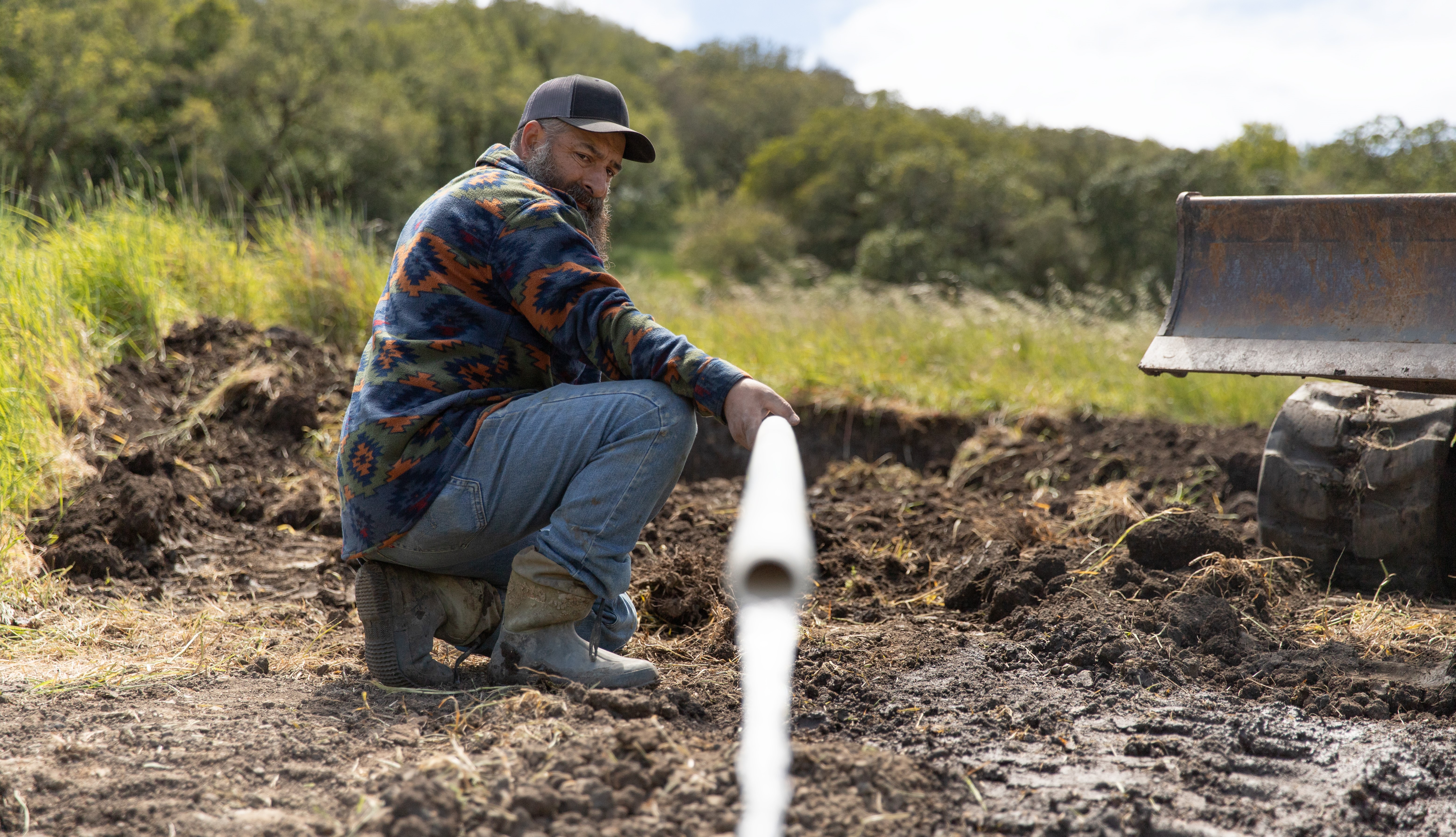 A farmhand adjusts an irrigation pipe in a muddy field.