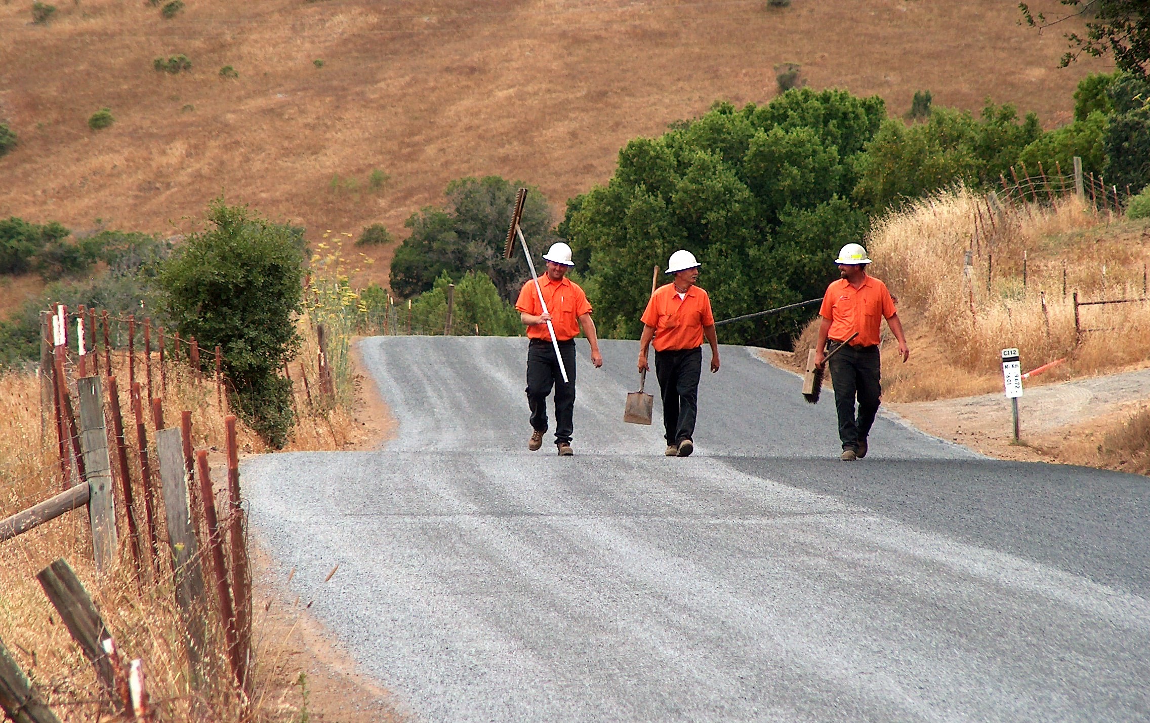 Three construction workers walk on a rural road that will be repaved.