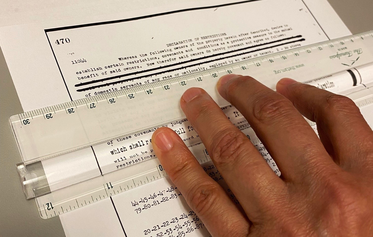 A closeup view of a person's fingers holding a ruler on a document that is being redacted.
