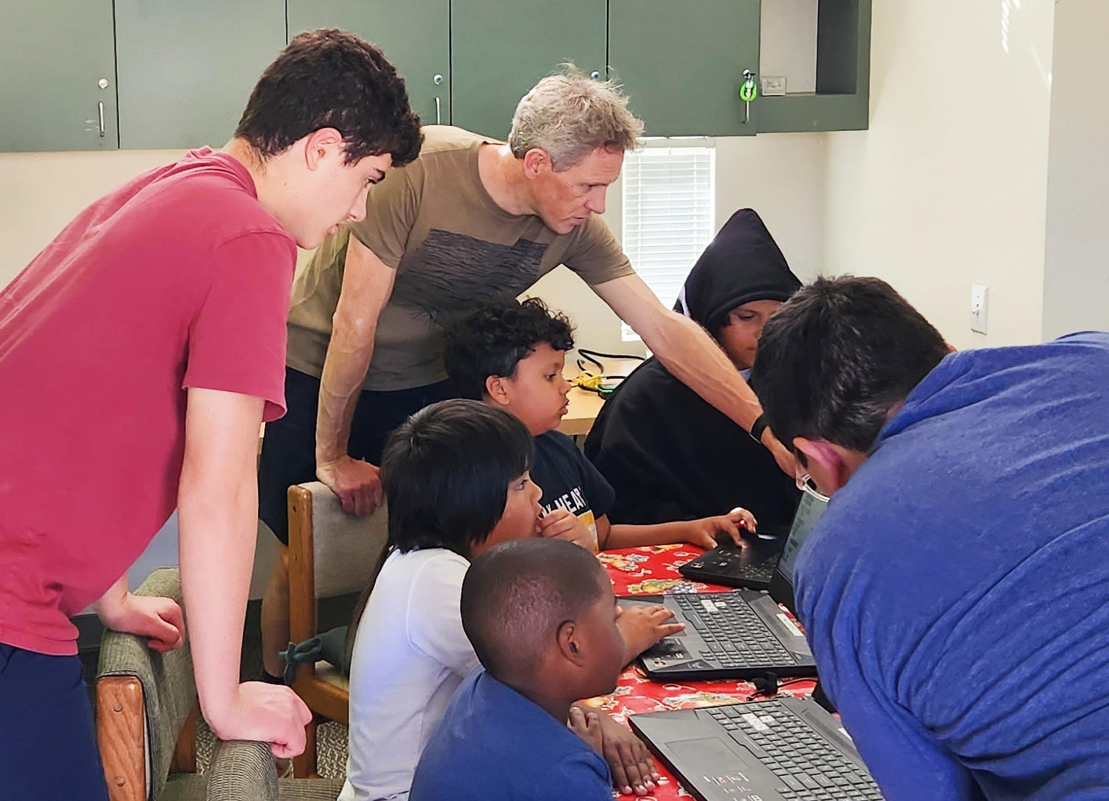 An instructor leans over and shows young kids something on a laptop computer.
