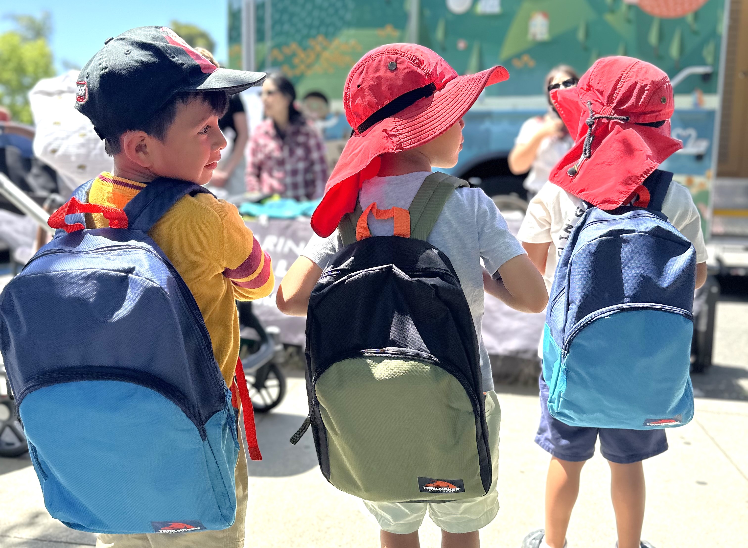 Three young boys wear a free summer backpack from the library.