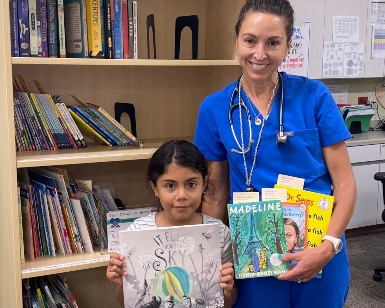 A child holds a book standing next to a female doctor inside a library.