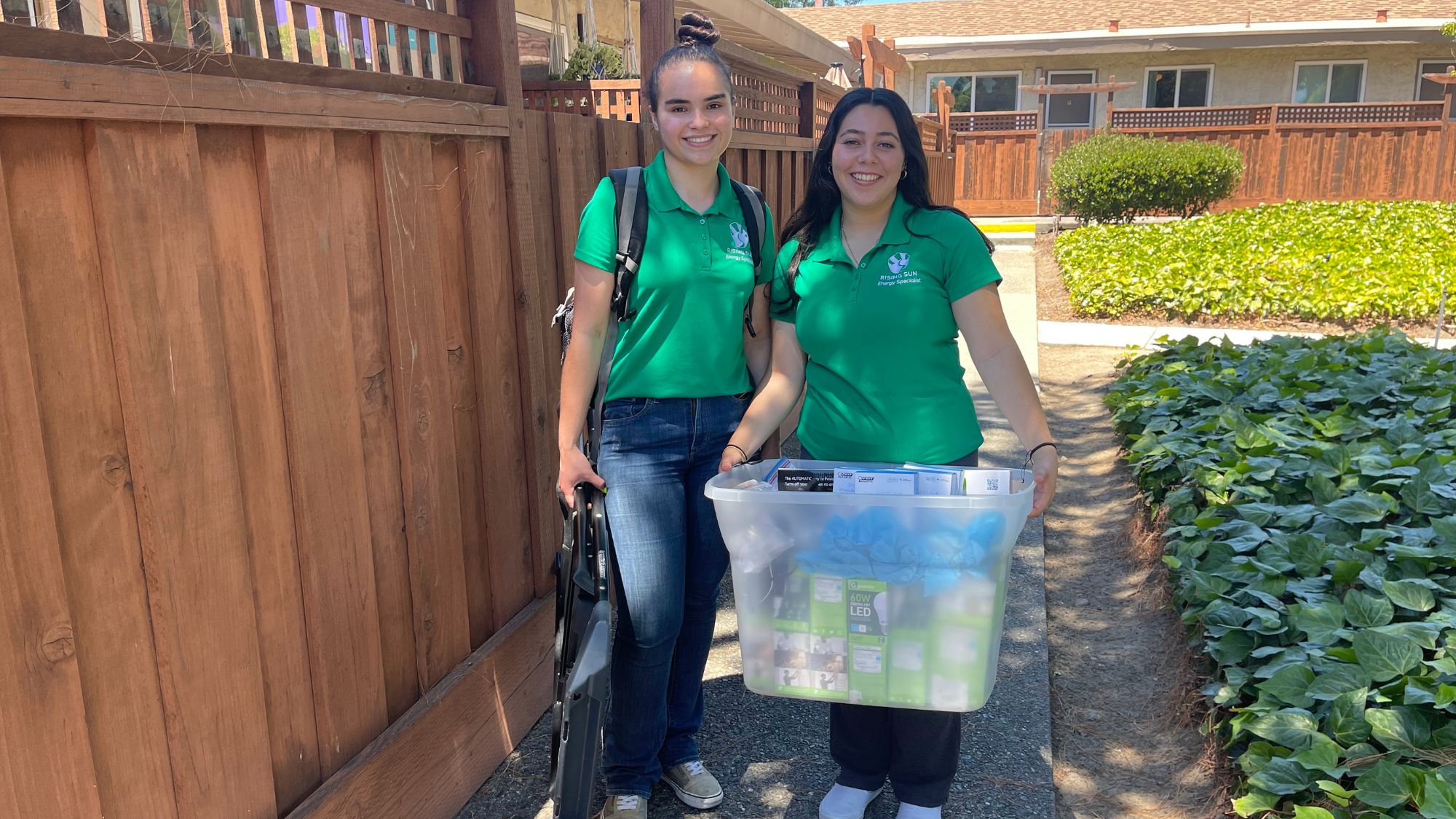 Two young women stand on a sidewalk and prepare to make a Rising Sun Green House Call.