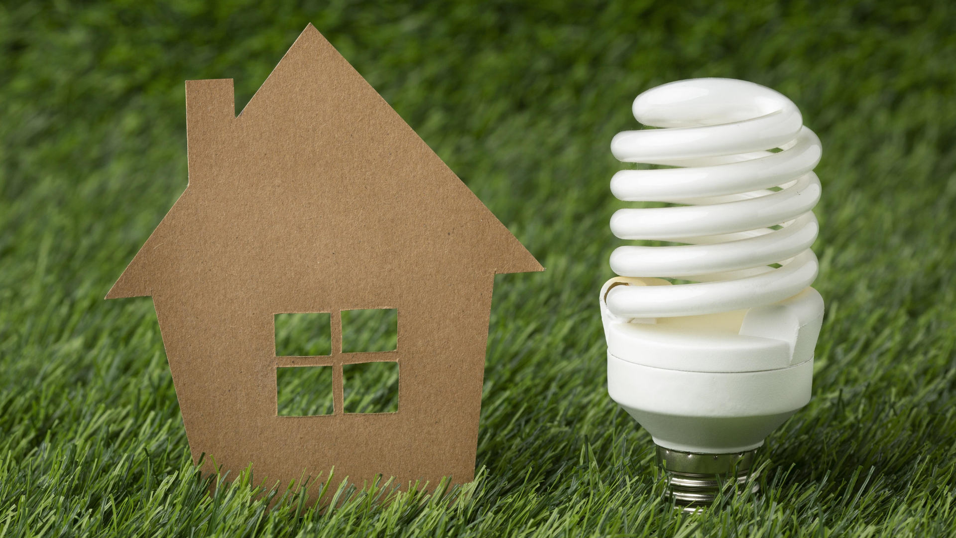 A cardboard cutout of a house sits next to an energy efficient lightbulb