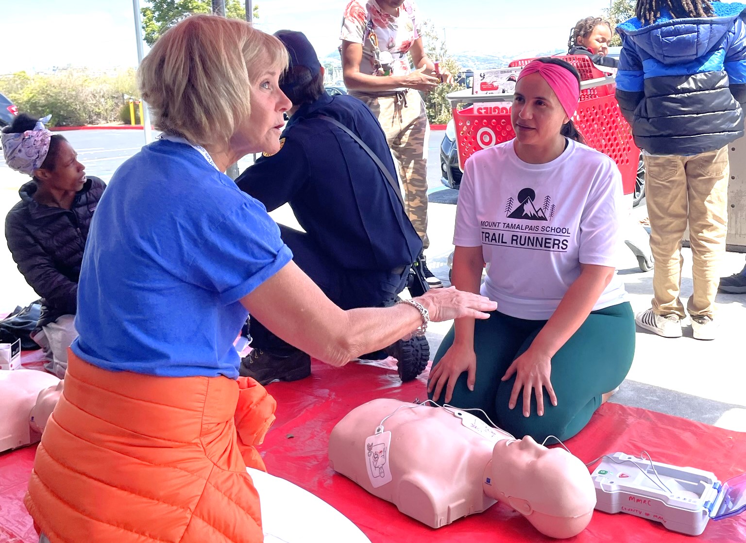 A woman describes CPR technique to another woman as both knee in front of a plastic human dummy.