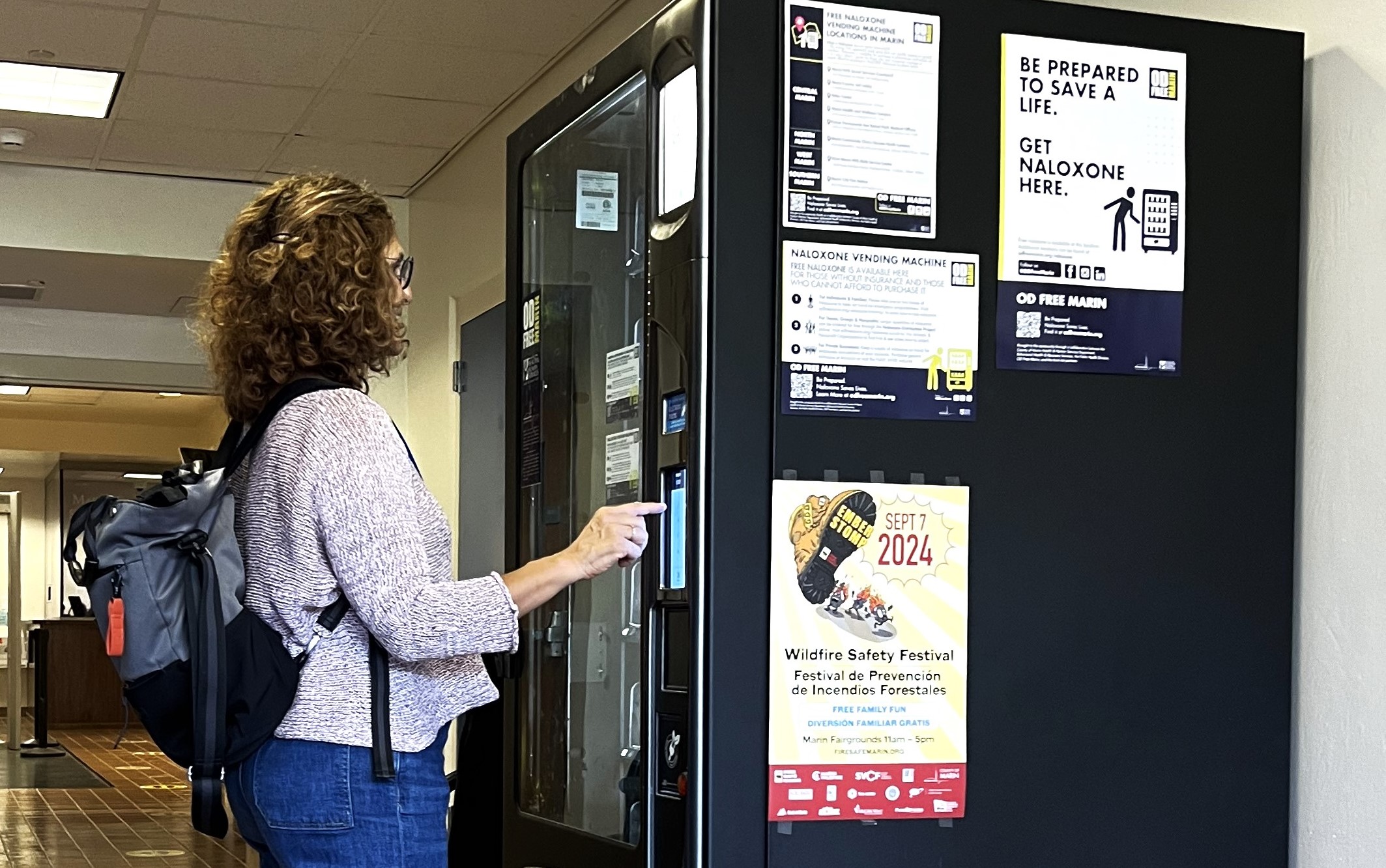 A woman stands in front of a naloxone vending machine and pushes a button.