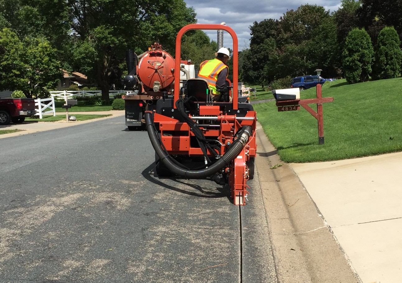 Fiber broadband installation equipment on a city street, cutting a gap in the pavement.