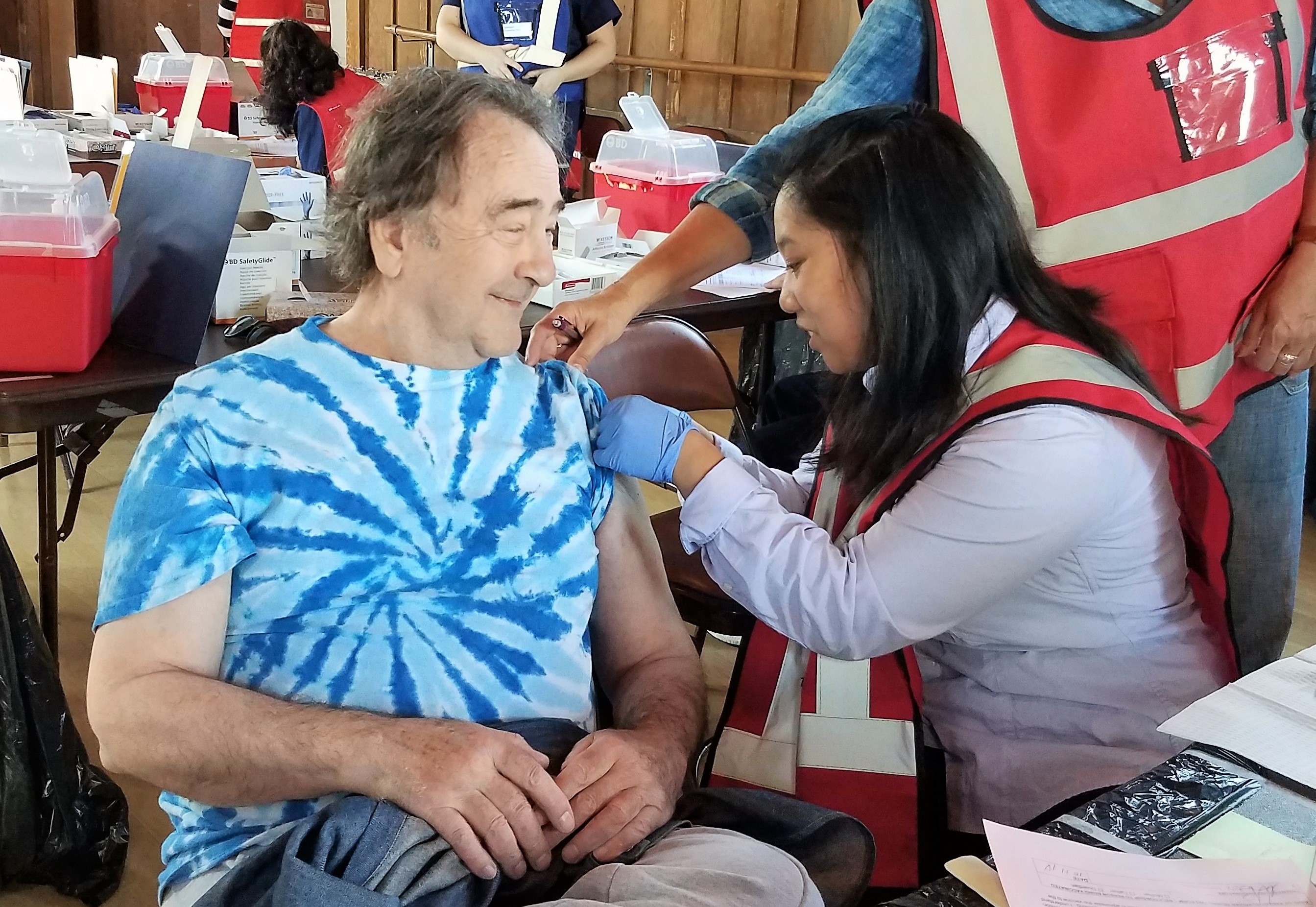 A man on the left smiles as he receives a vaccine from a female nurse on the right.
