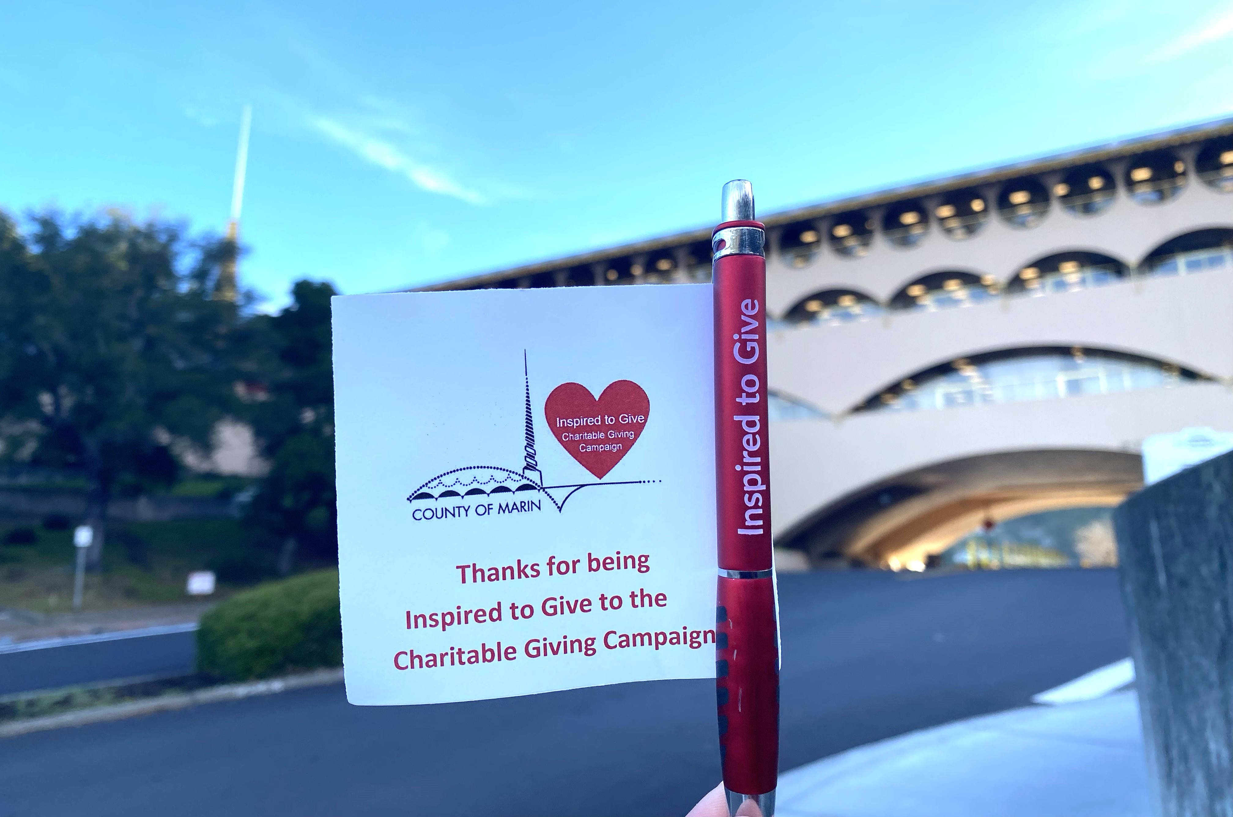 A person's hand holds up a pen and note about the donation campaign outside the Civic Center.