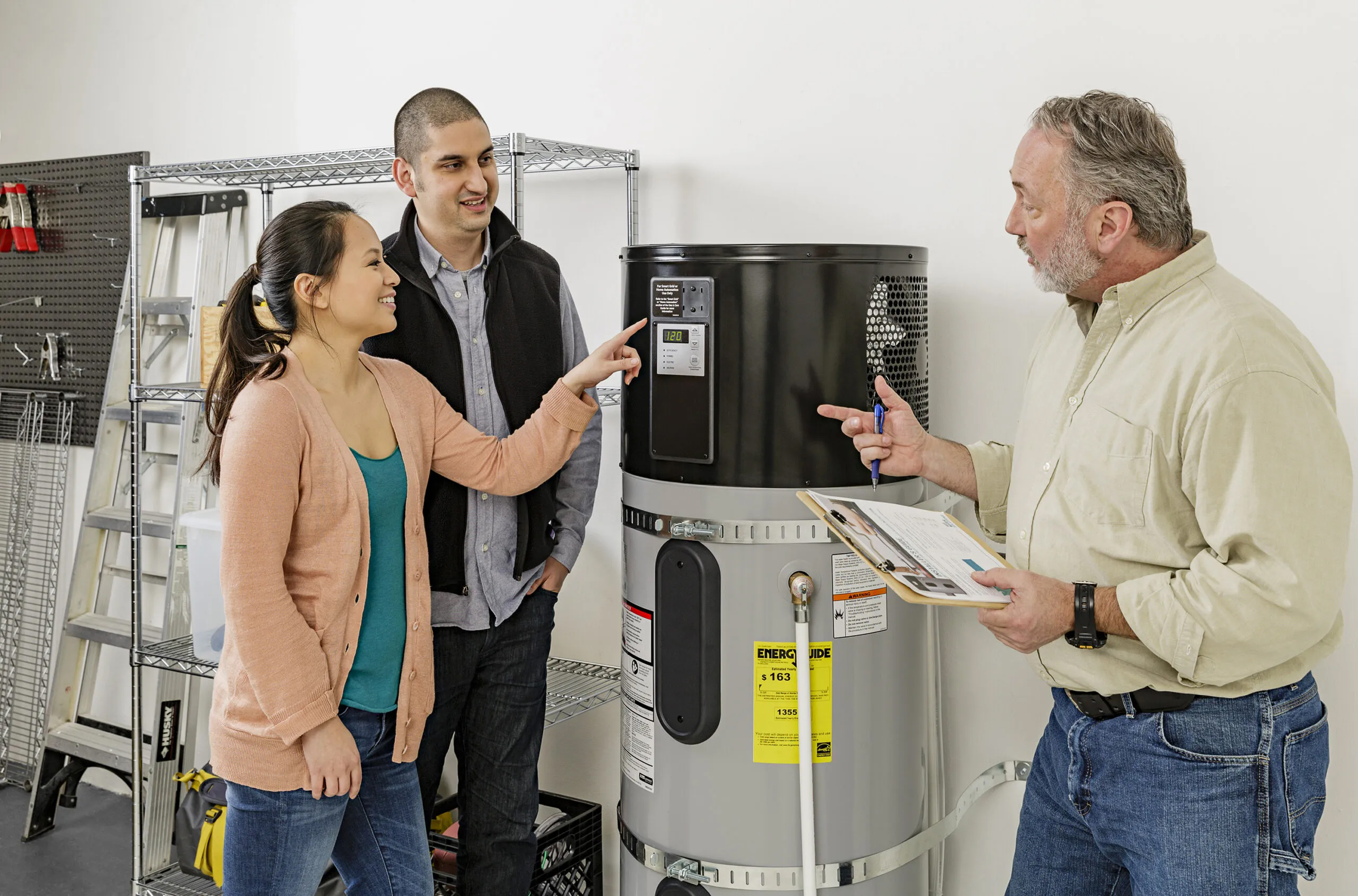 Three people speak while standing next to an installed heat pump.