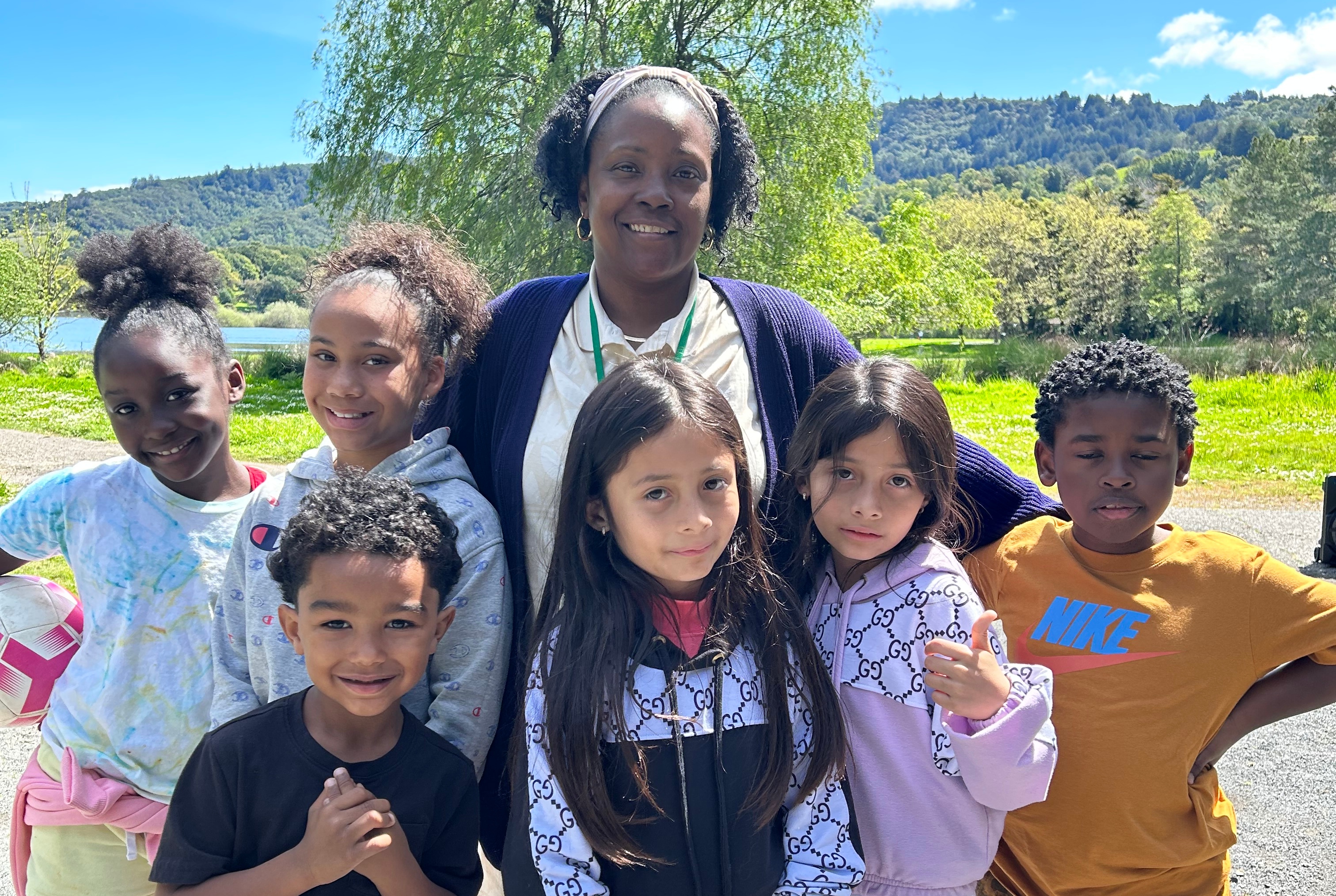 A group of kids and a mentor smile at a park.