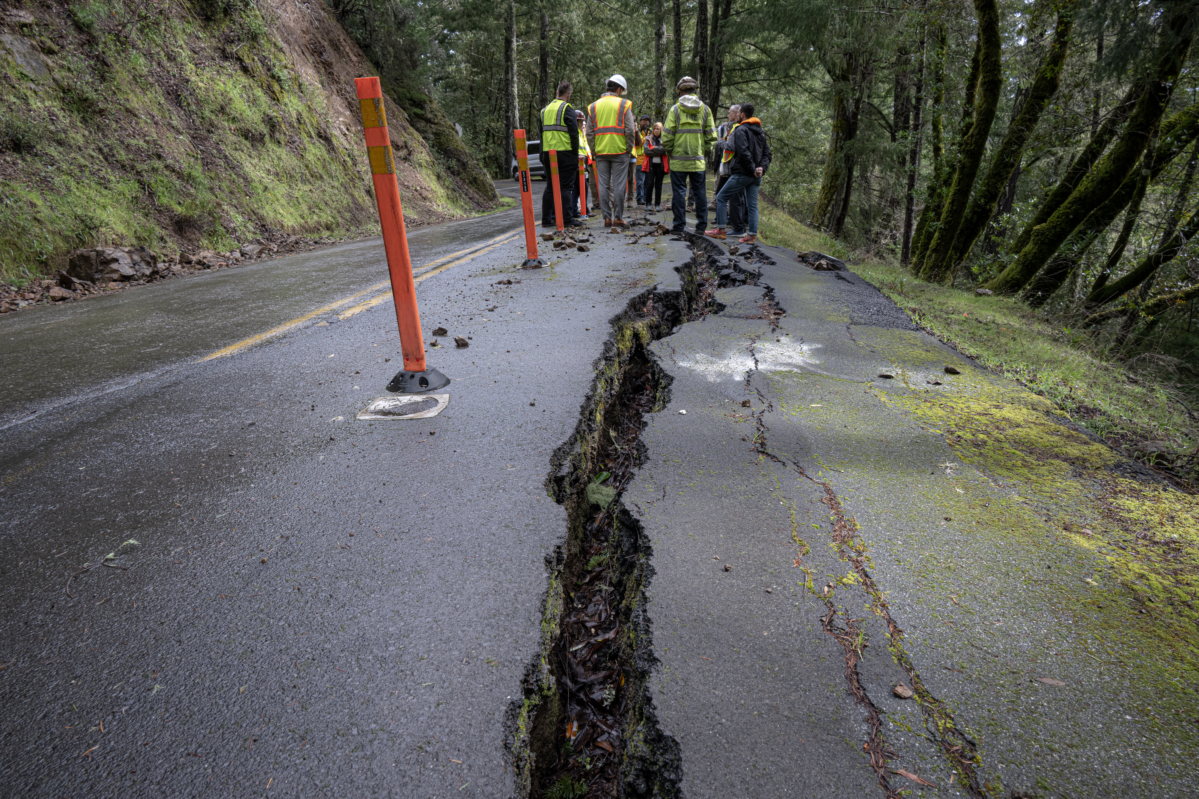 A closeup view of cracks in a road and emergency responders evaluating the problem.