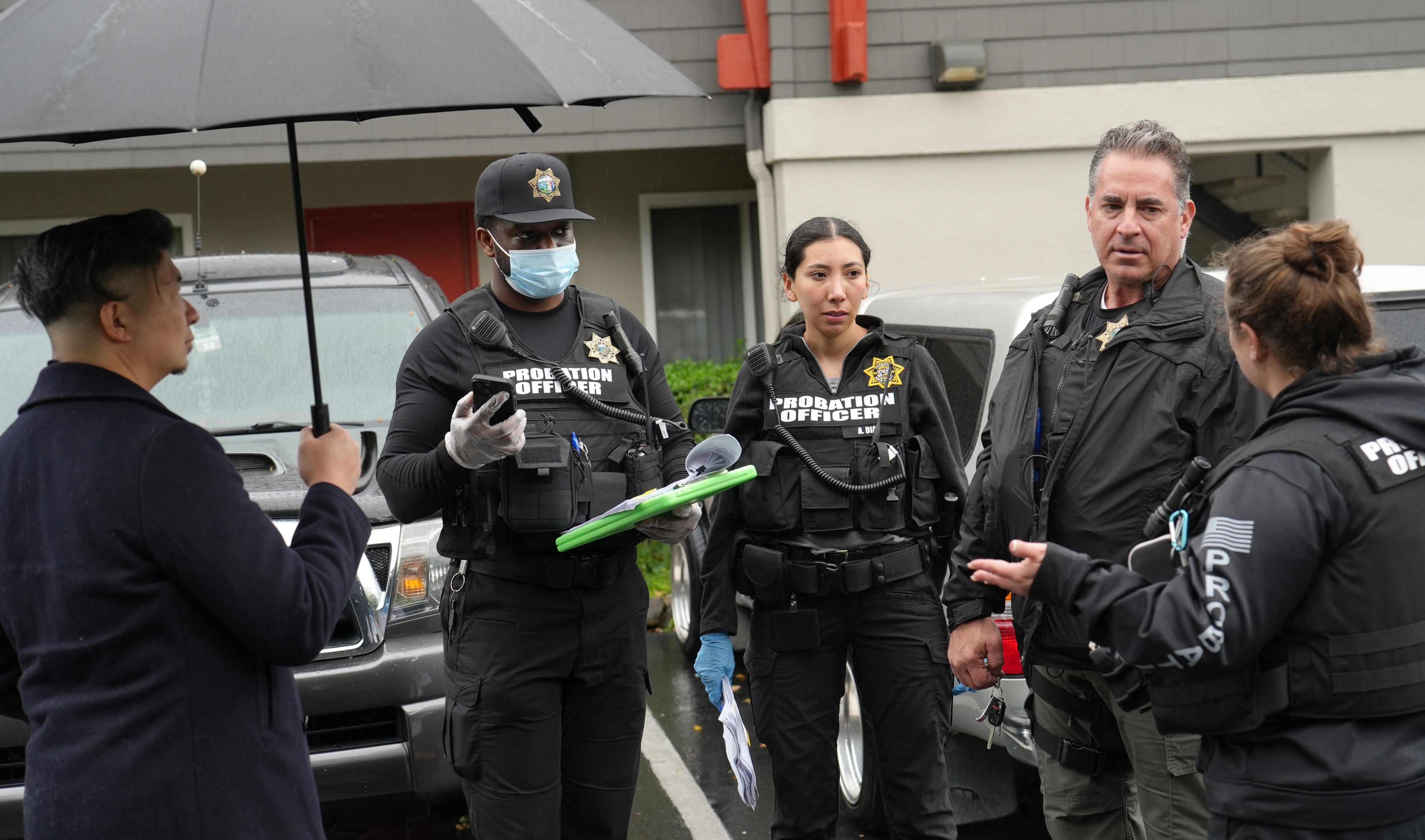 Five law enforcement officers confer in a parking lot before knocking on a probationer's door.