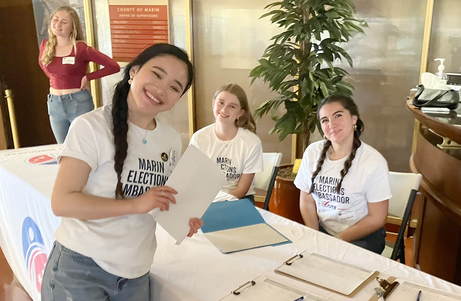 Three teenage girls smile at the Youth Town Hall front table.