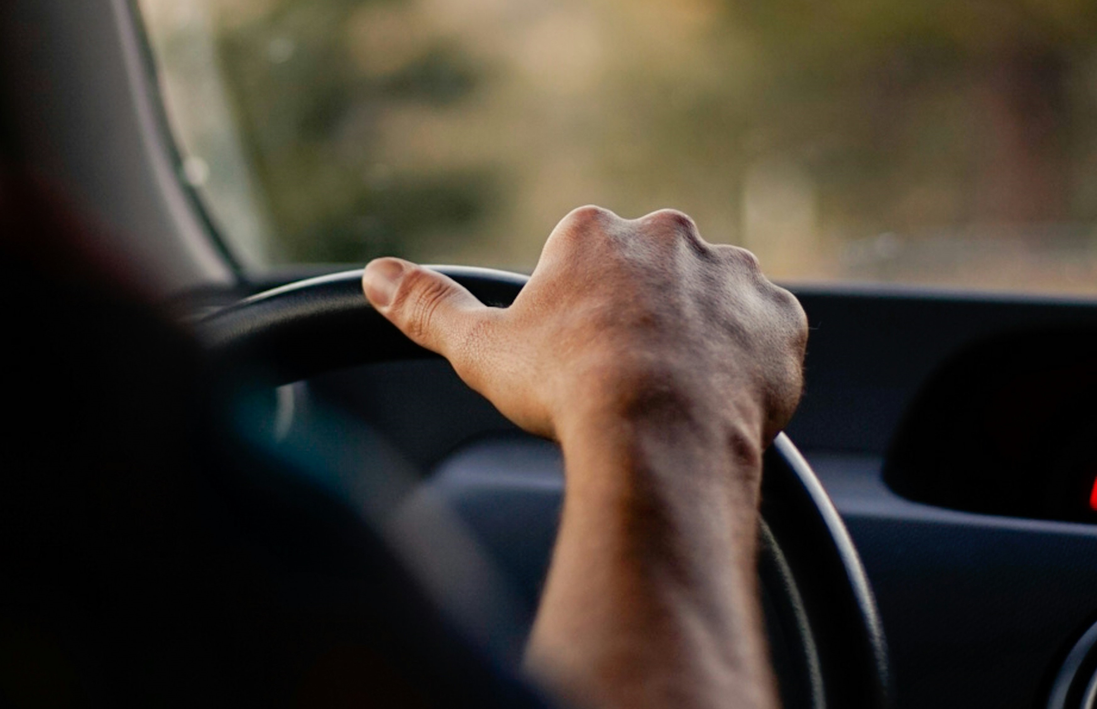 A closeup view of a person's hand on a vehicle steering wheel.