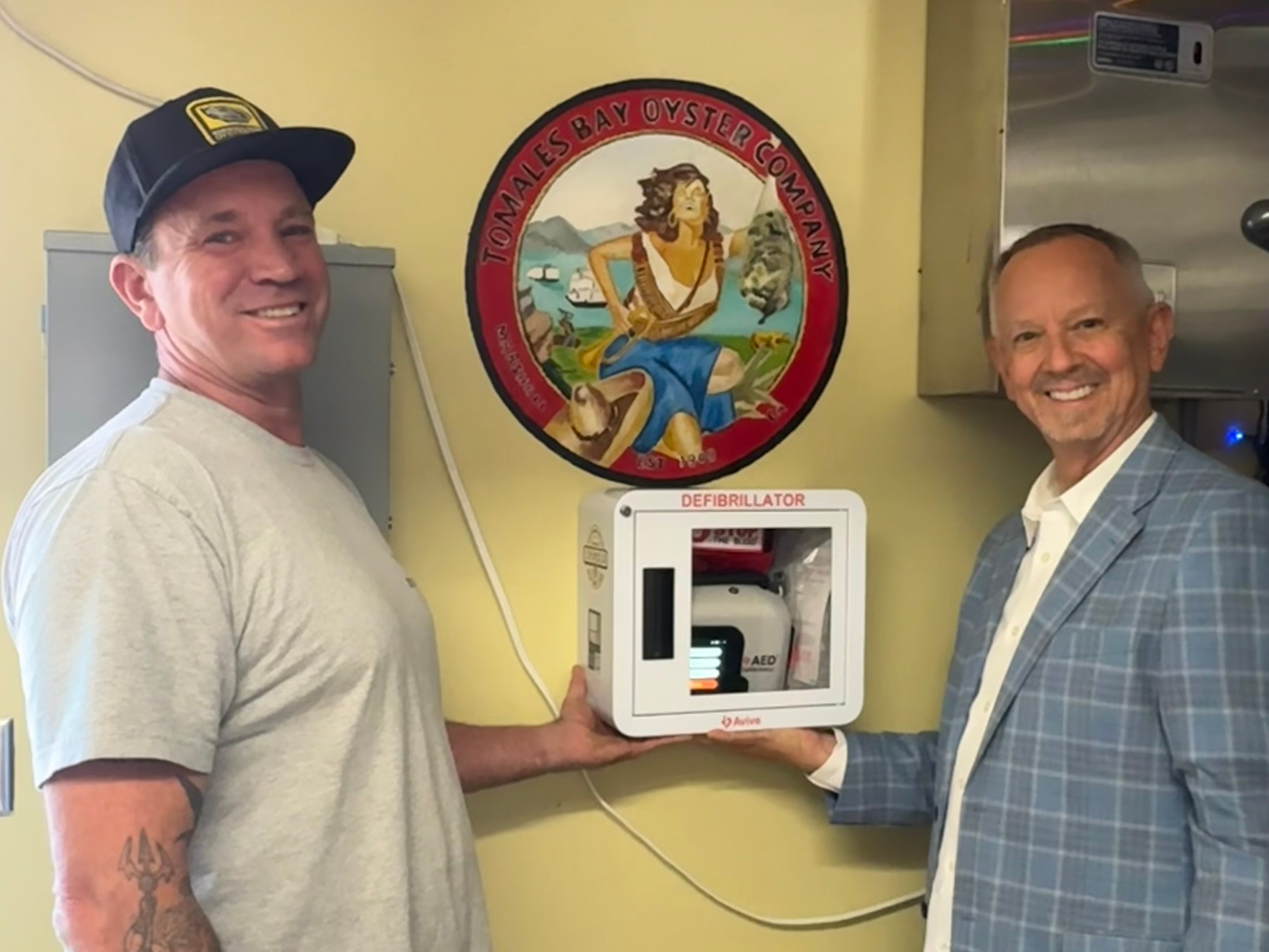 Two men pose with an AED (defibrillator) at a store.
