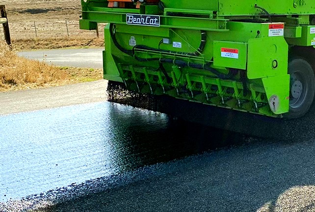A closeup look at heavy machinery laying down tar on a road to fix the pavement. 