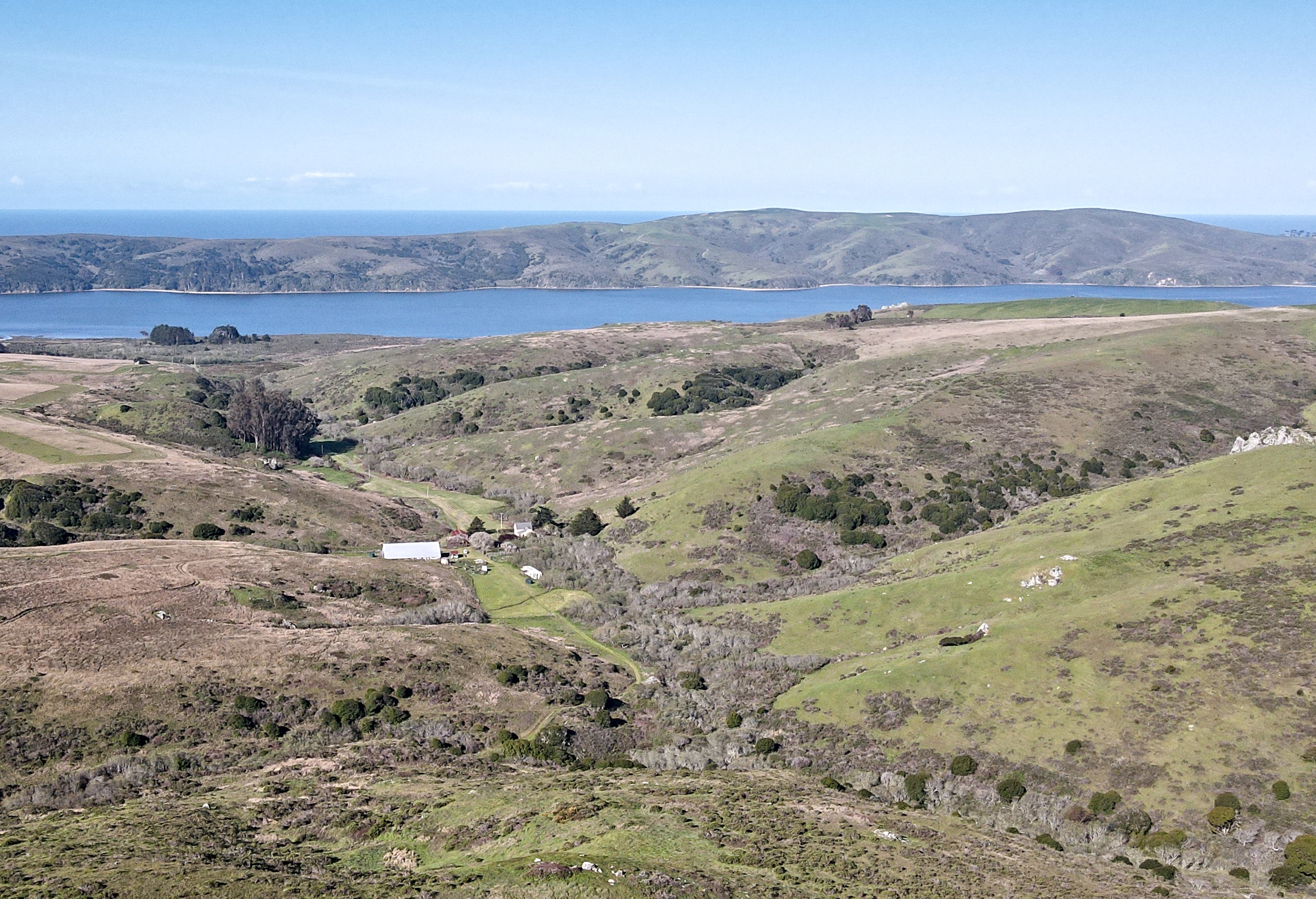 Hilltop view looking down on a distant ranch with Tomales Bay behind it.