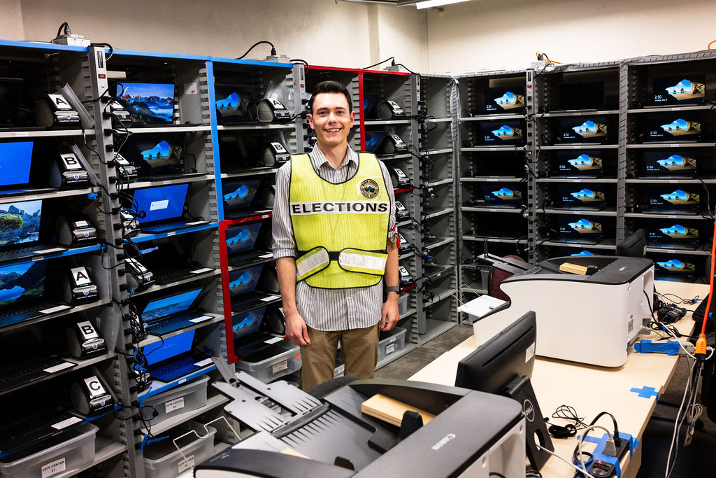 An elections worker poses with a cabinet full of laptop computers to be used on election day.