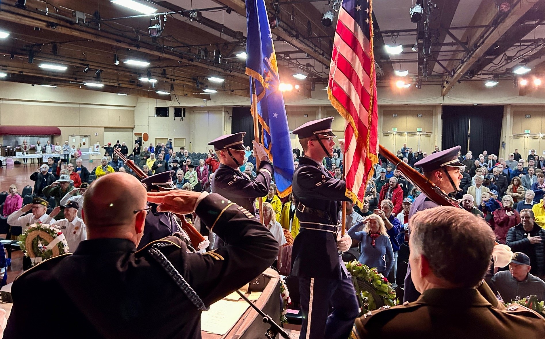 Members of an honor guard carry flags next to military veterans who are saluting.