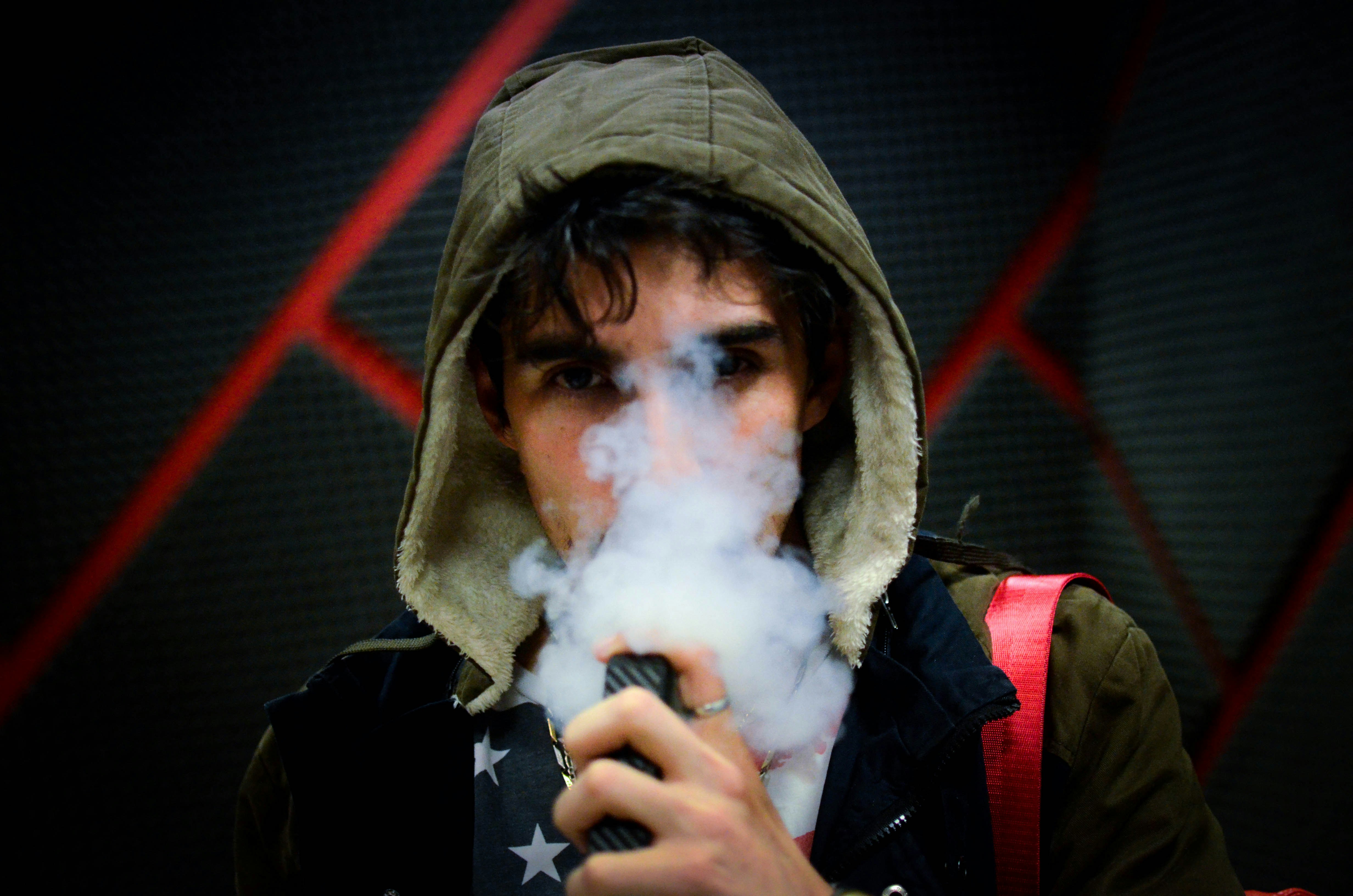 A man in a hoodie is vaping, with smoke coming from his mouth