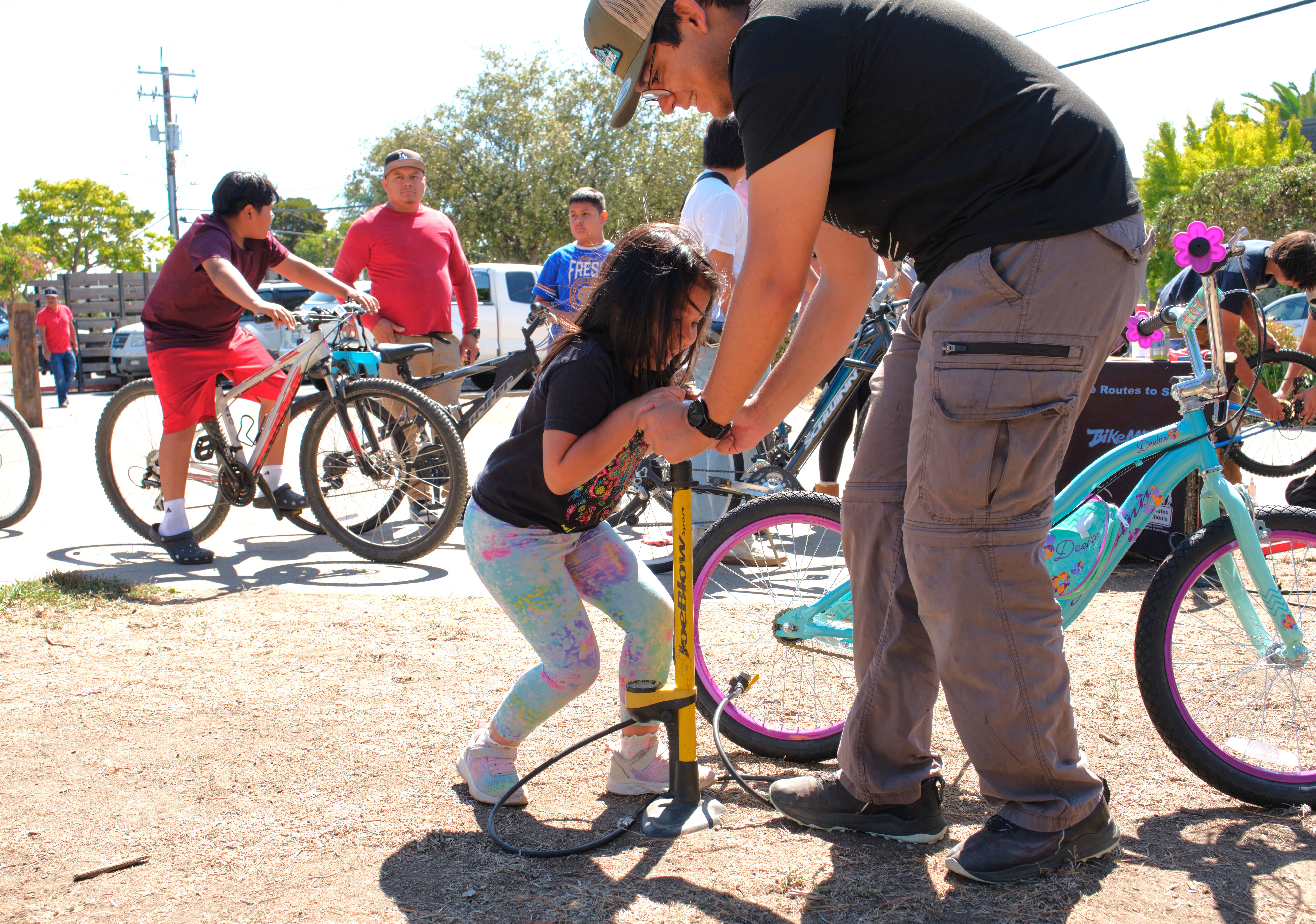 A man helps a young girl pump up a bike tire.