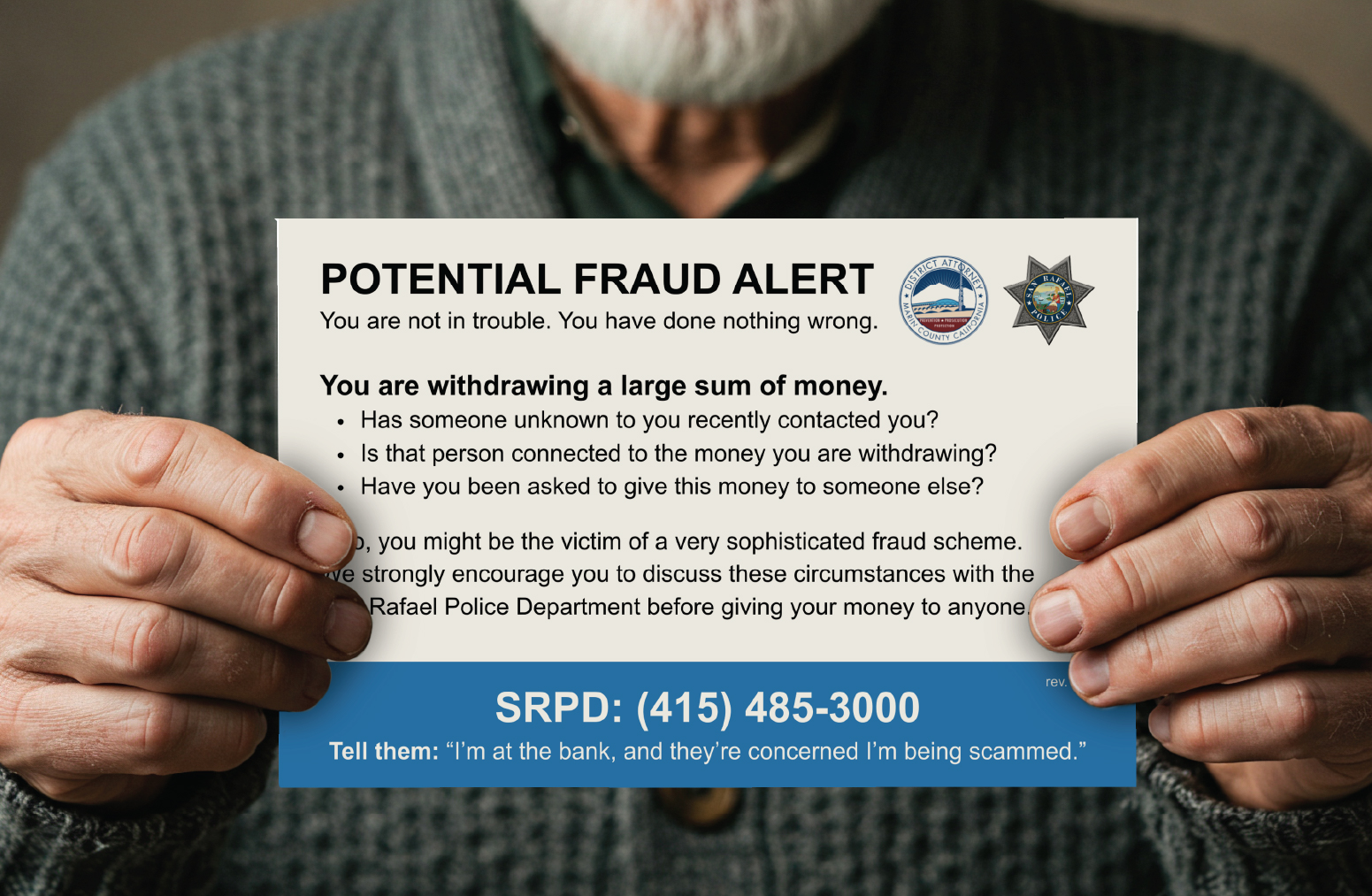 A person's hands are shown holding up a warning card about financial fraud.