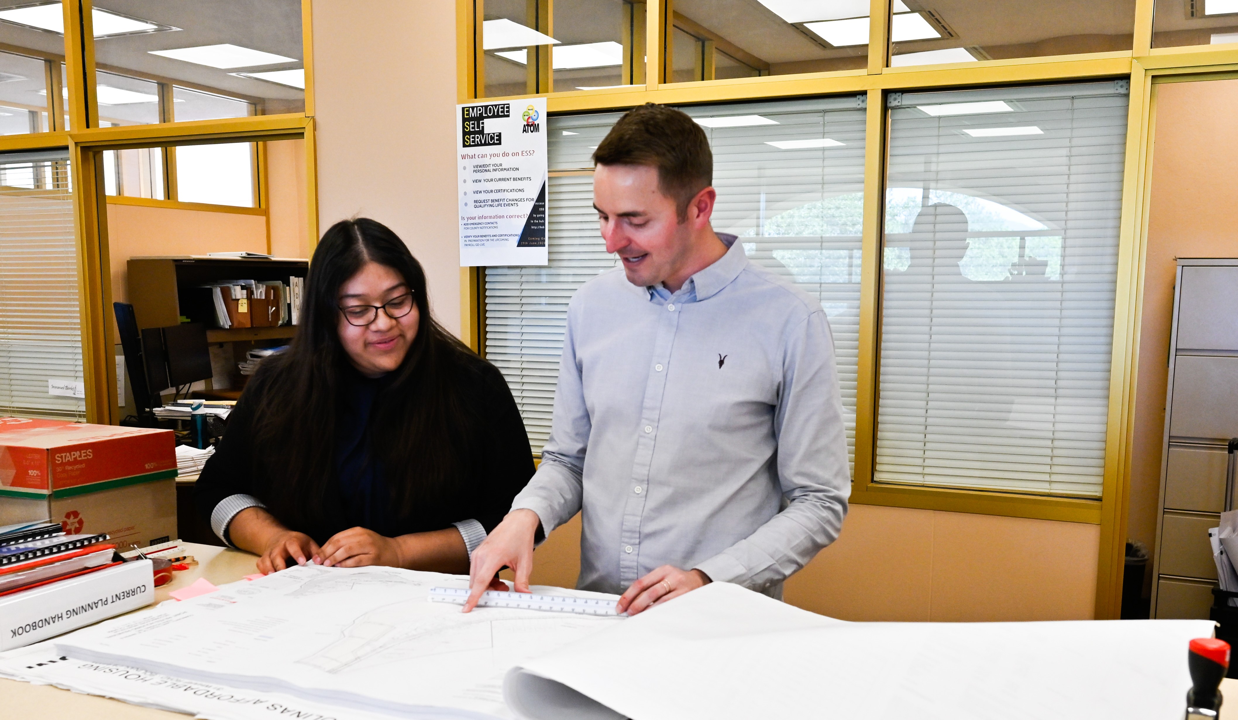 Two members of the County Planning Division speak as they look at paper plans on a table.