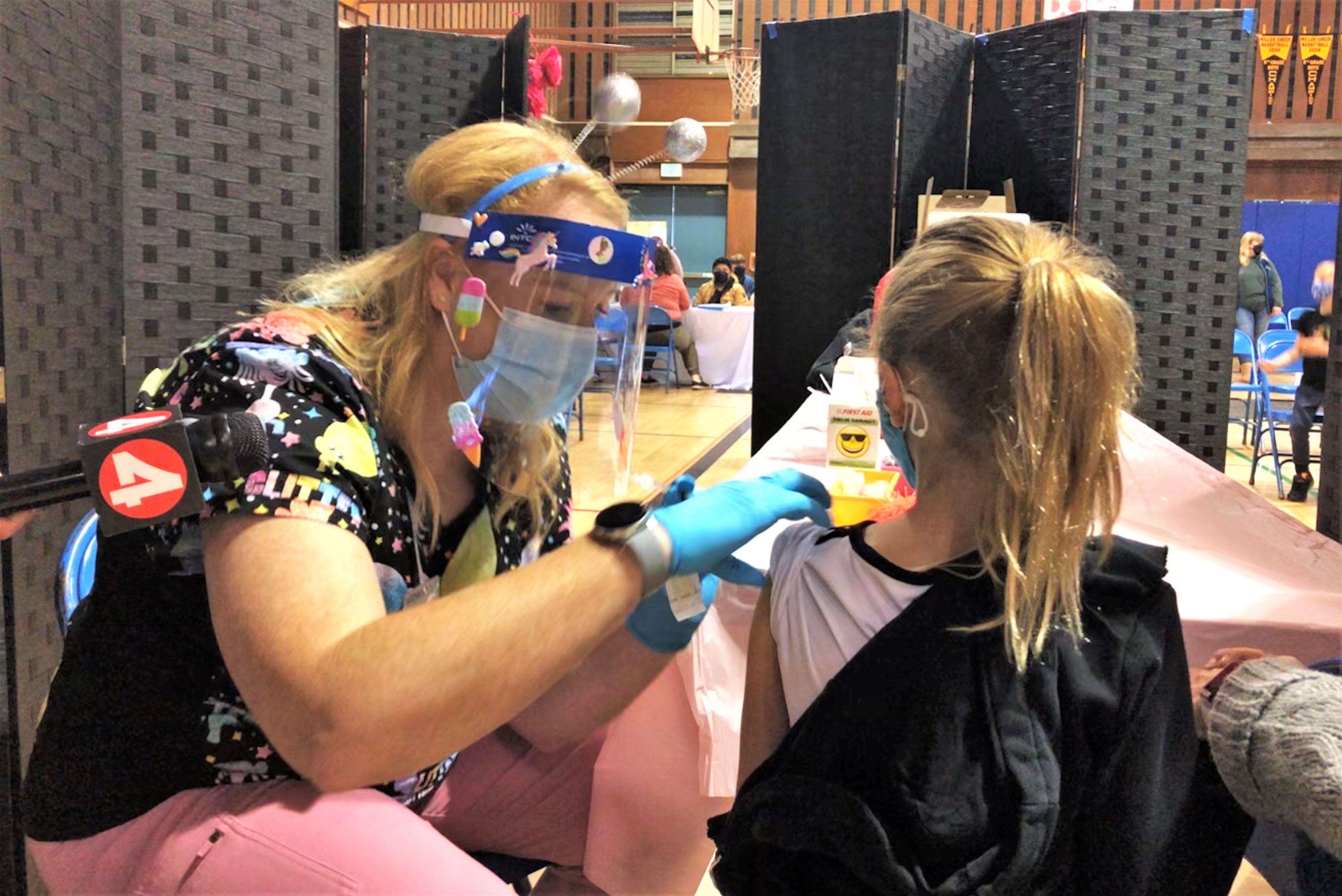 A female nurse on the left gives a shot to a young girl on the right.
