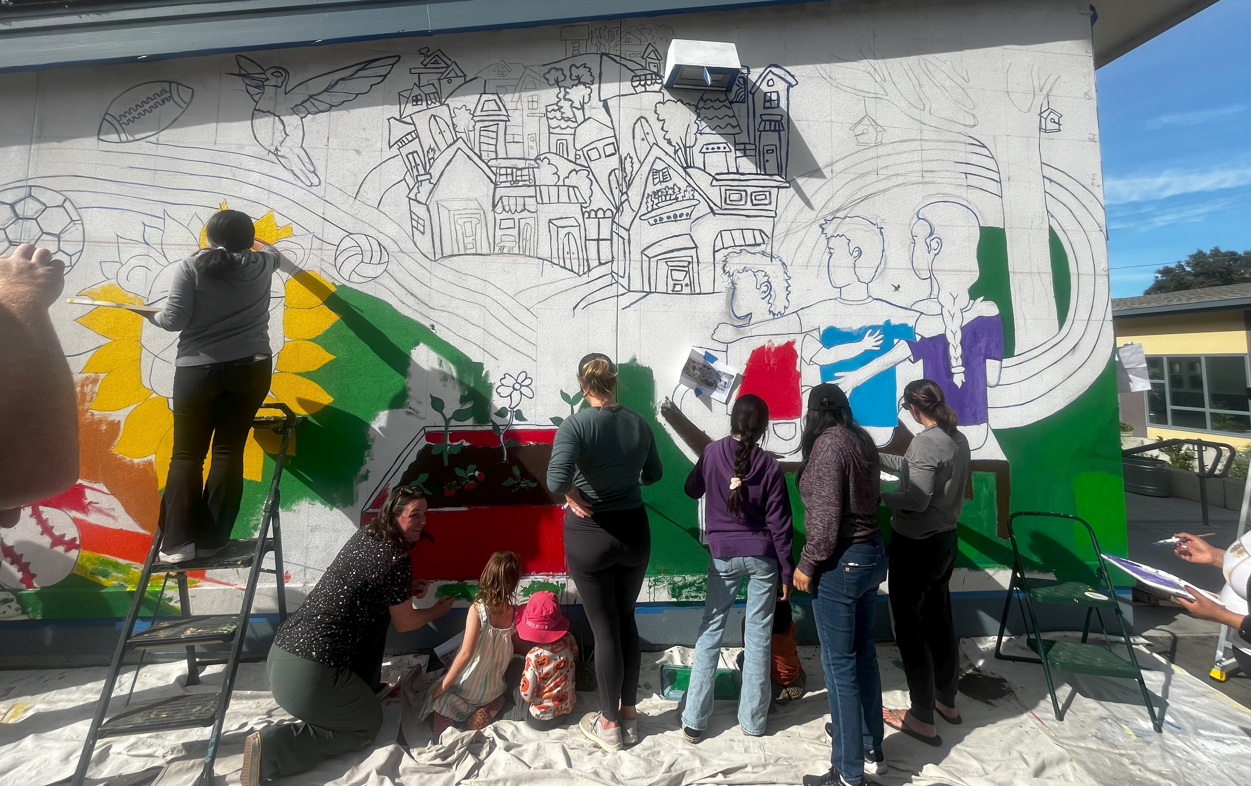 Several teen artists work on a mural on the side of a building.
