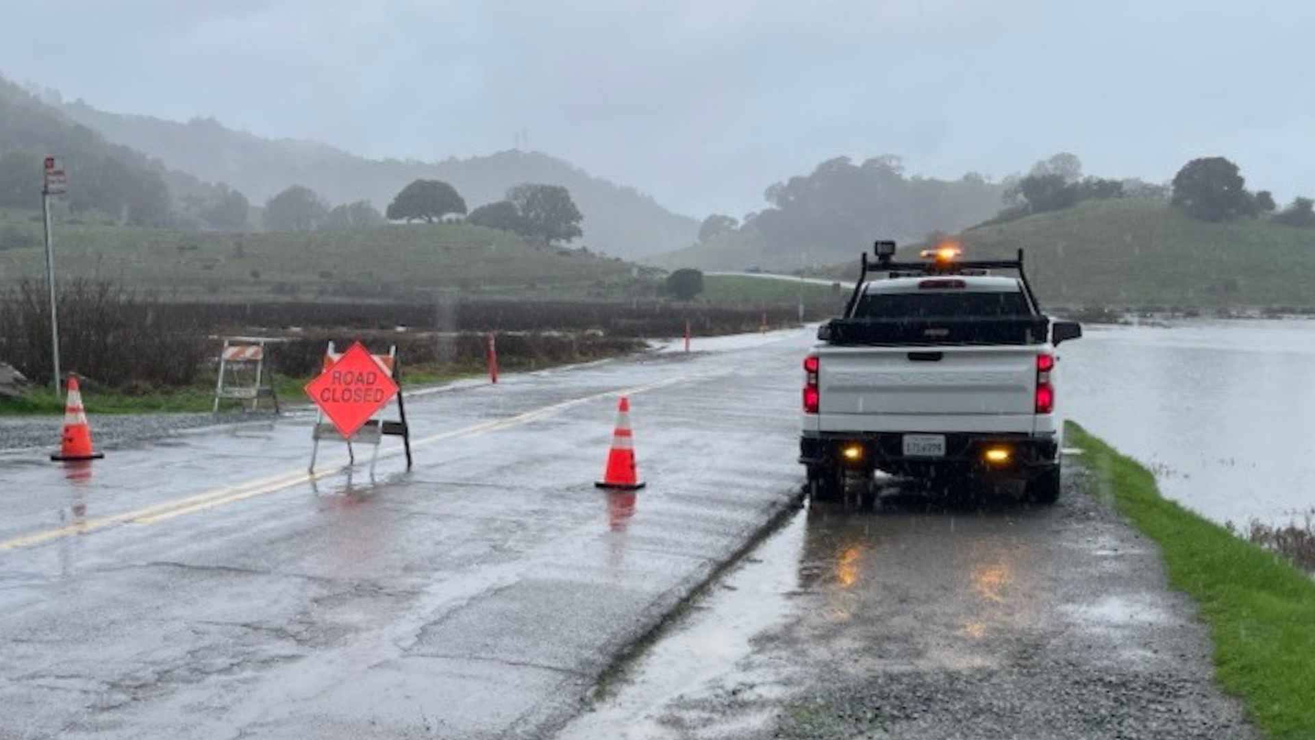 A DPW vehicle is partially blocking a road that is flooded and closed.