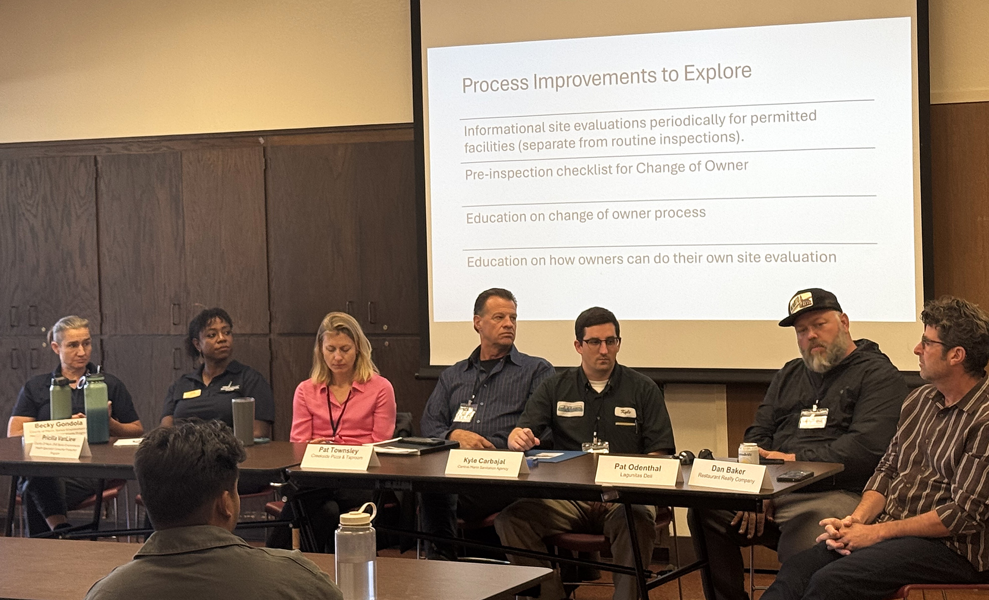 Six people sit at a table and listen during a community discussion about the food program.